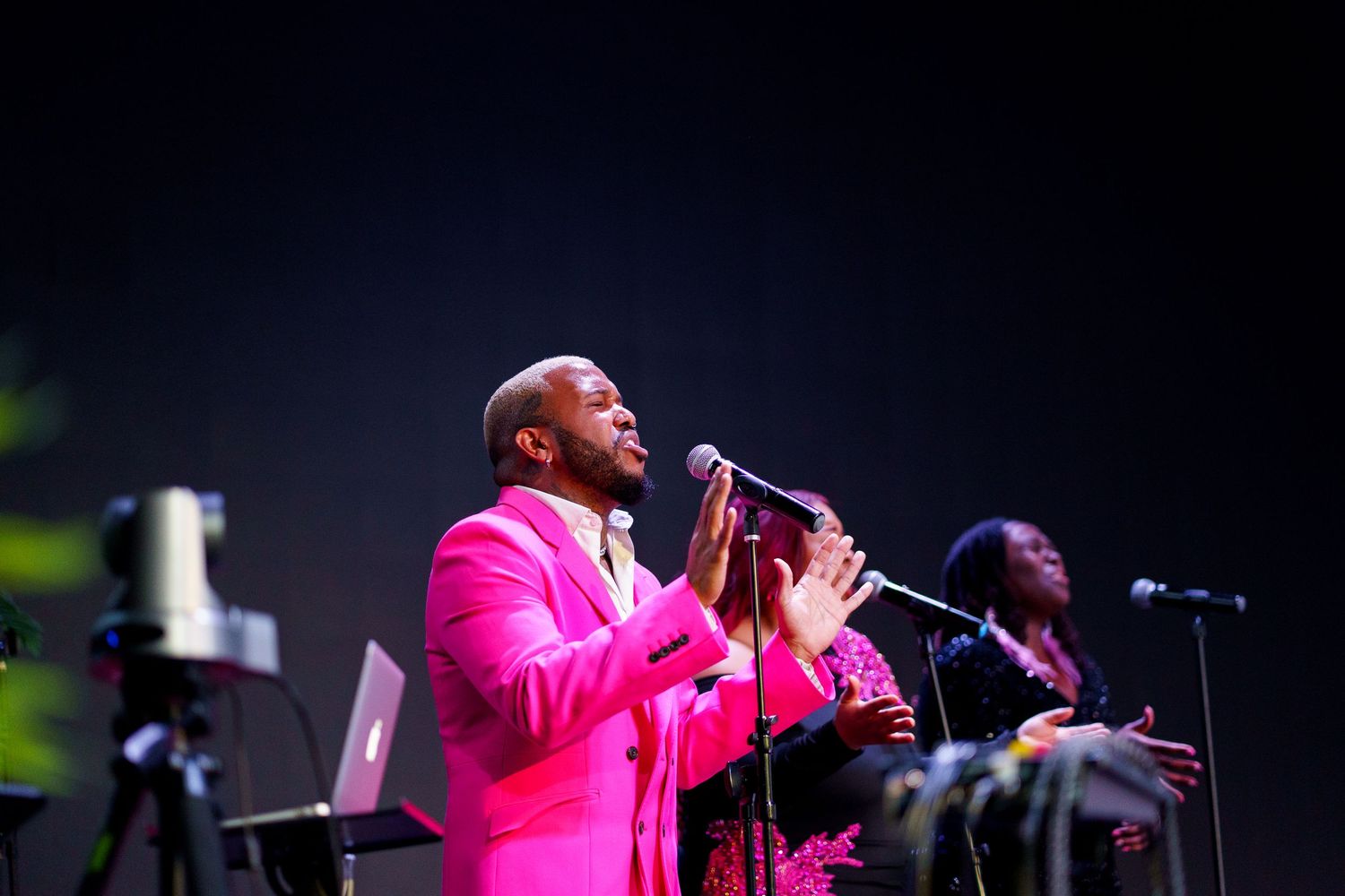 A performer in a bright pink suit sings passionately on stage during a concert performance.