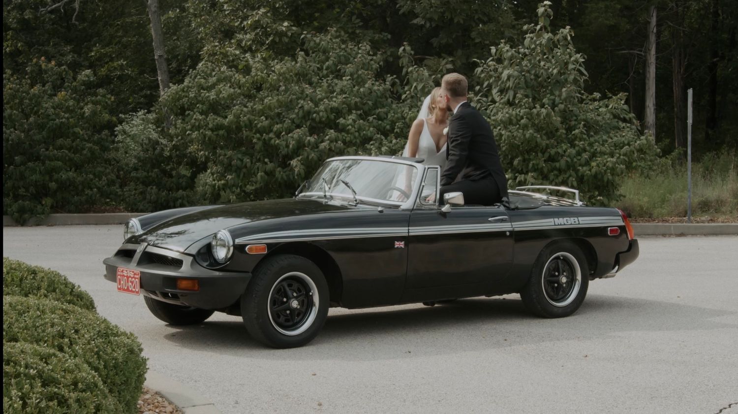 Newlyweds riding in a classic black MGB convertible on their wedding day.