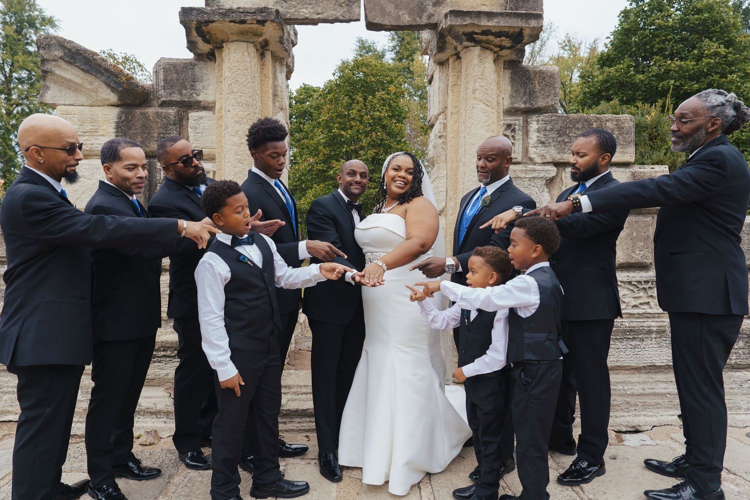Wedding guests form a joyful dance circle at an outdoor reception near a historic stone building.