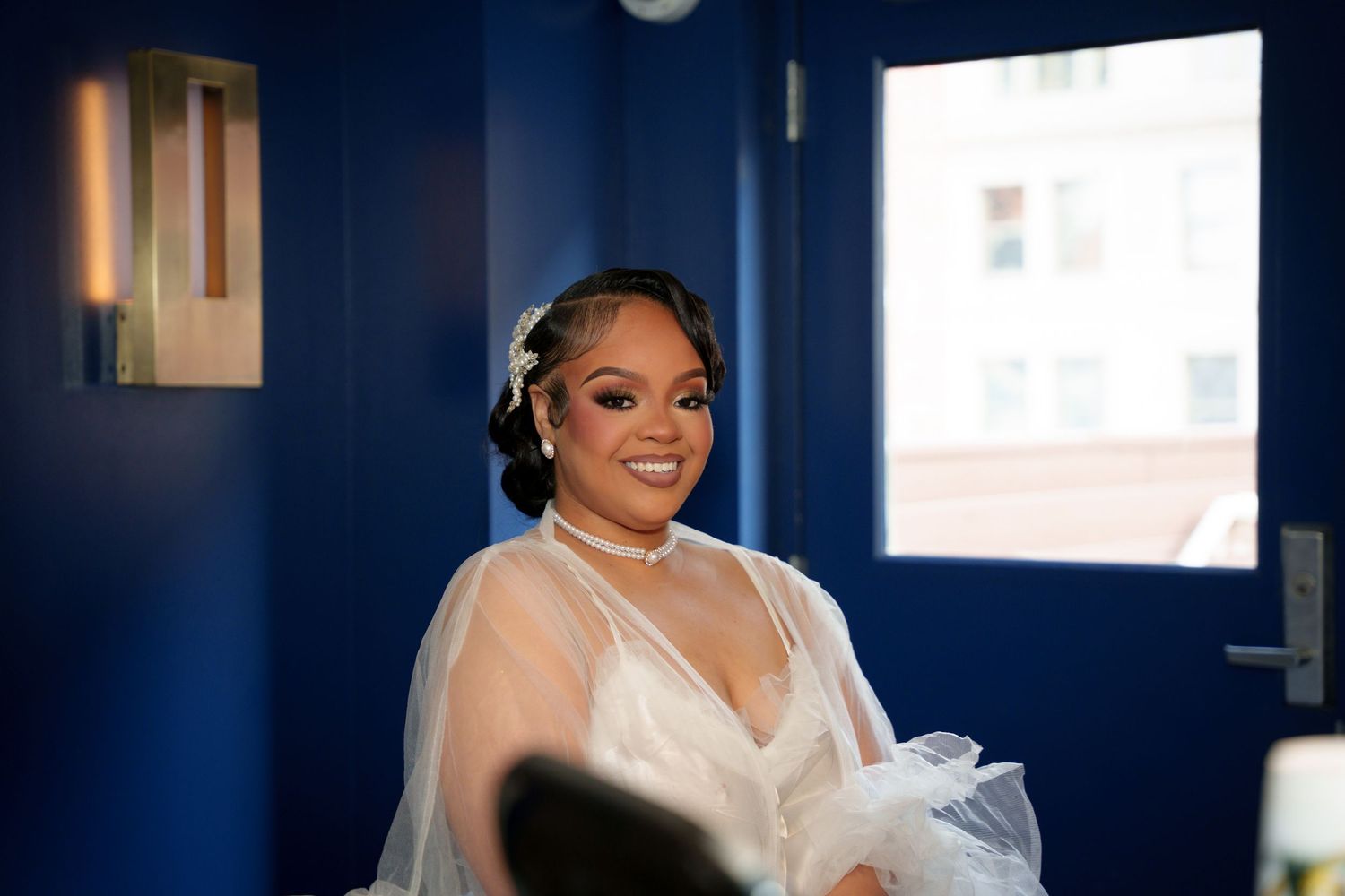 Wedding party members pose in a room with dark blue walls and natural lighting.