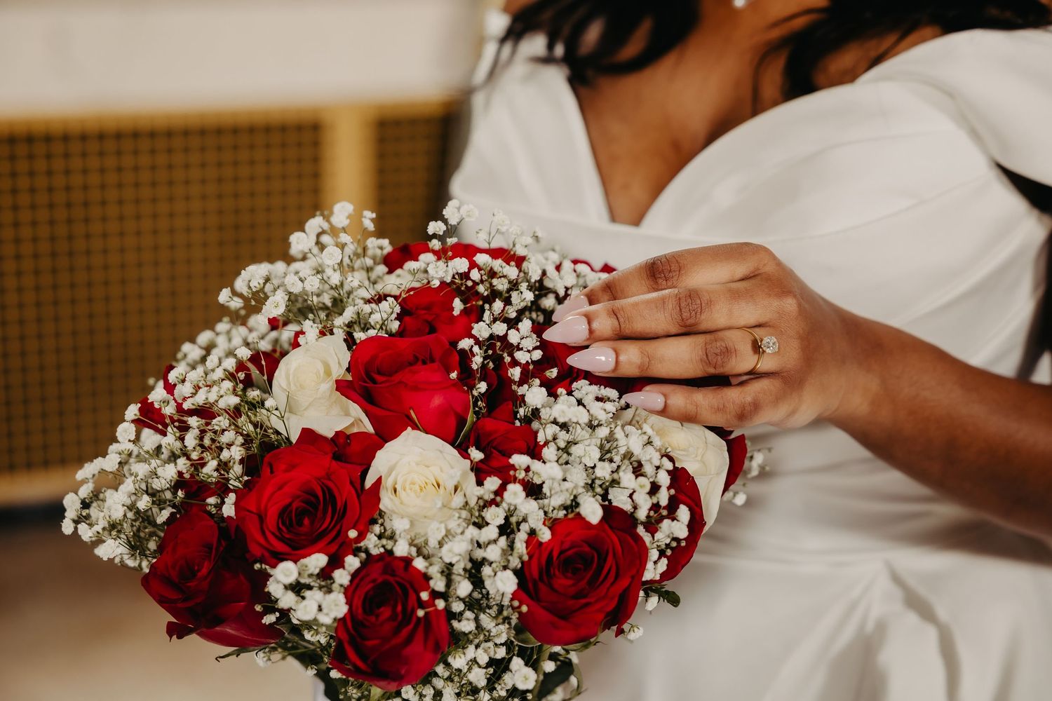 A stunning wedding bouquet featuring red roses and baby's breath held by hands in a white dress.