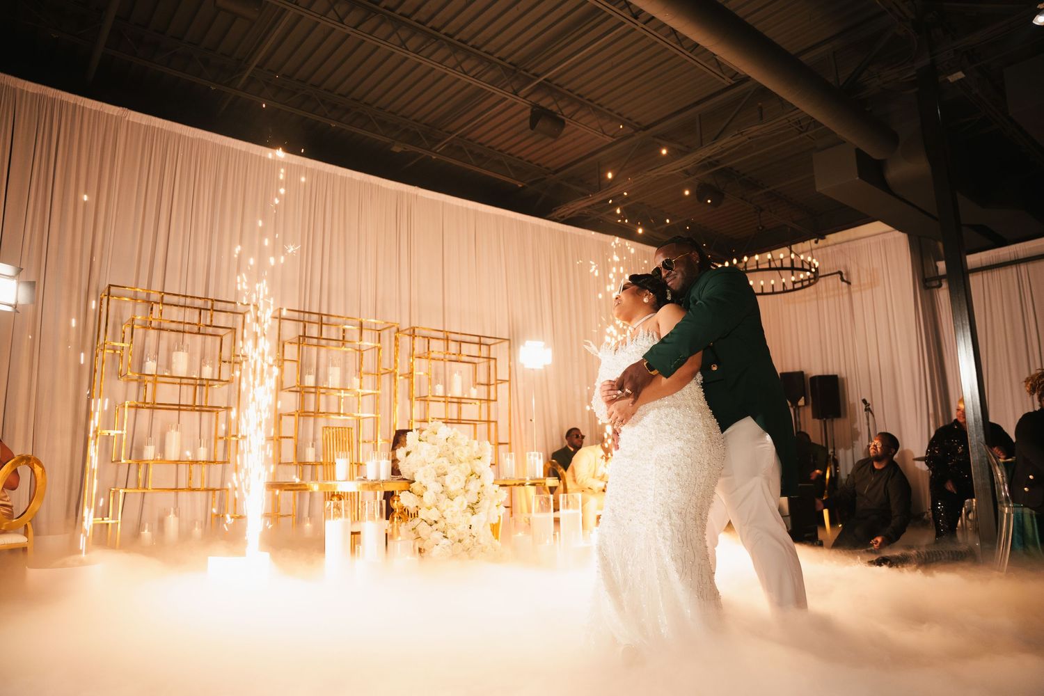 A couple performs their first dance on a foggy dance floor with elegant gold geometric decor in the background.