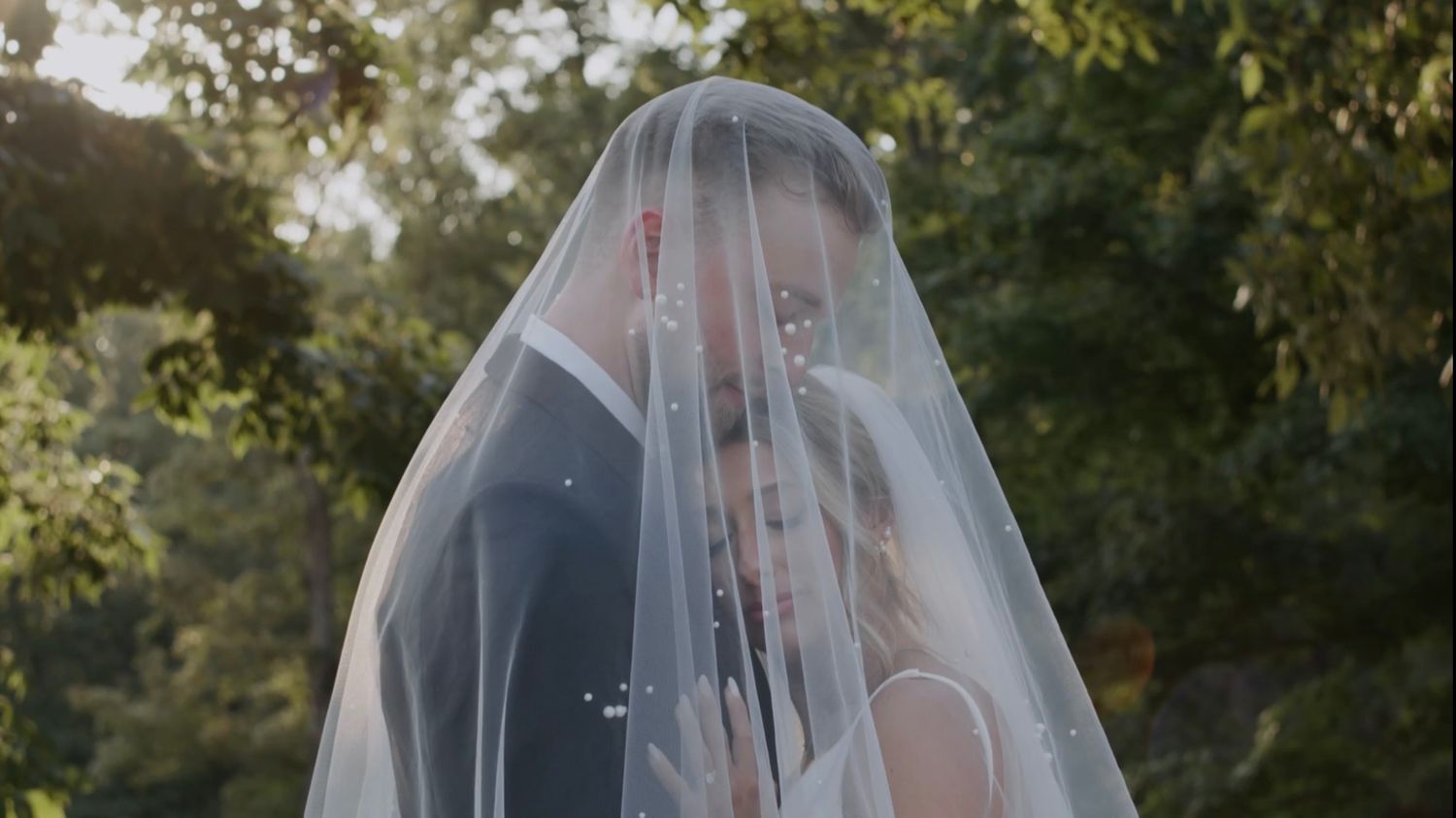 Romantic wedding moment captured through a delicate white veil against green foliage.