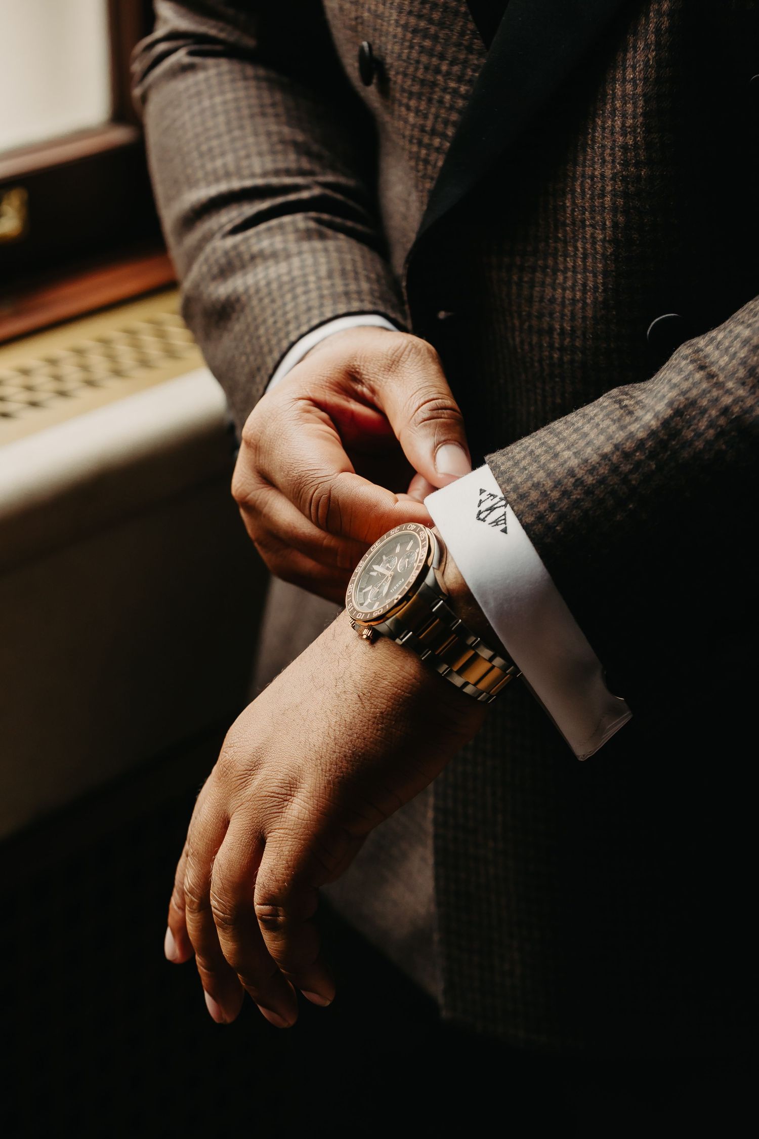 Close-up of hands adjusting a watch cuff in a textured grey suit.
