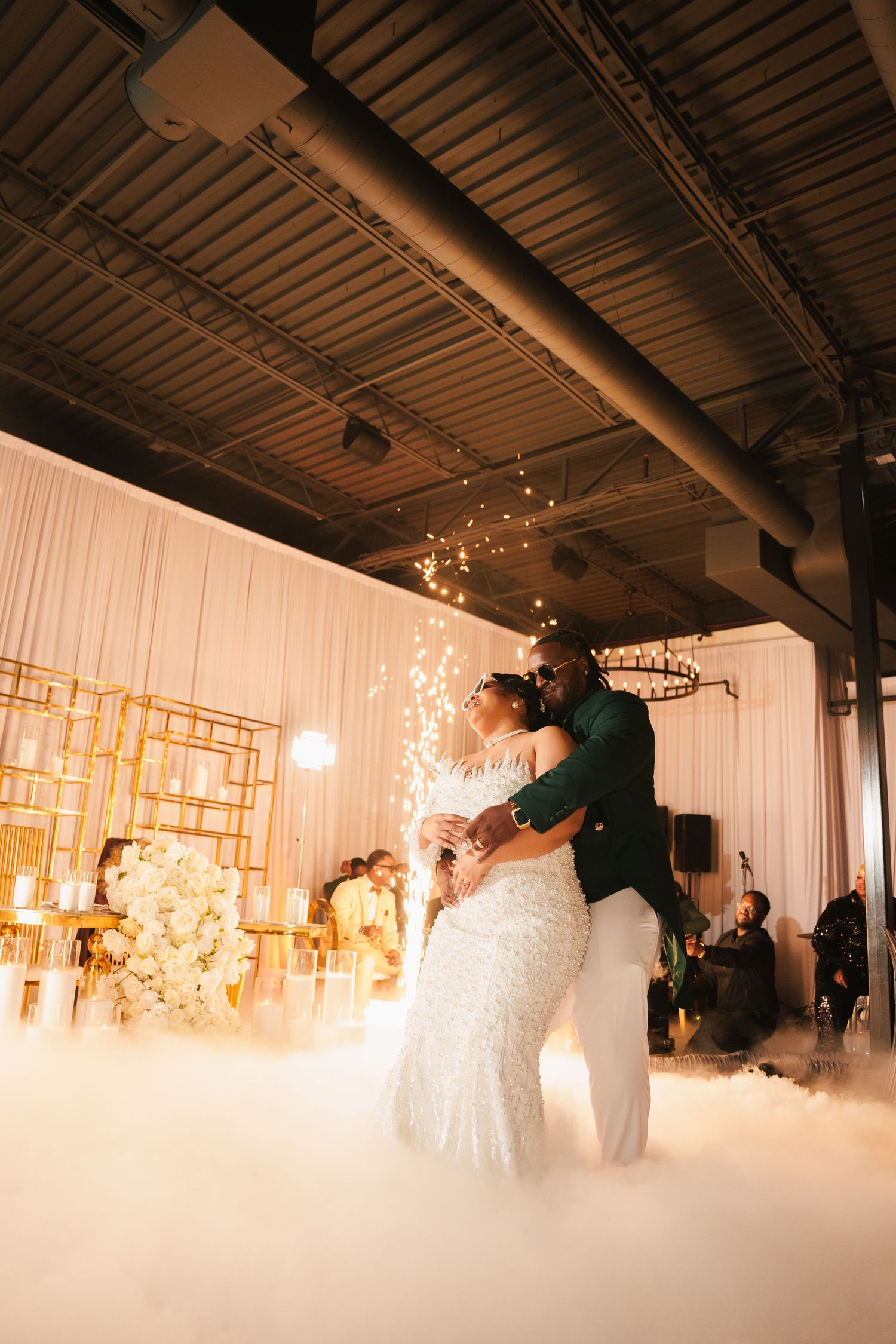 A couple shares their first dance surrounded by fog and twinkling lights at an elegant indoor wedding reception.