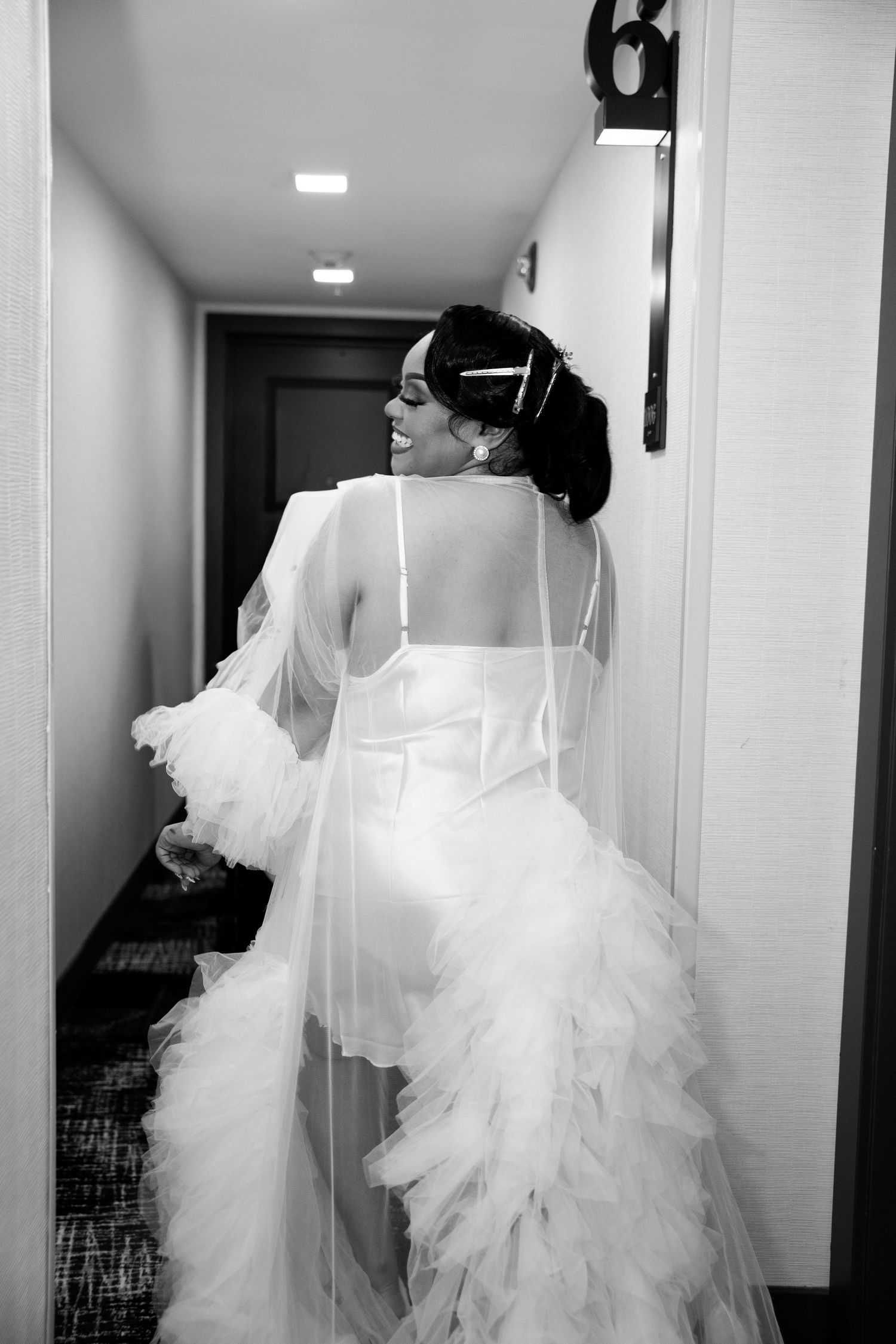 Flowing white wedding dress train trails behind in a bright hallway.