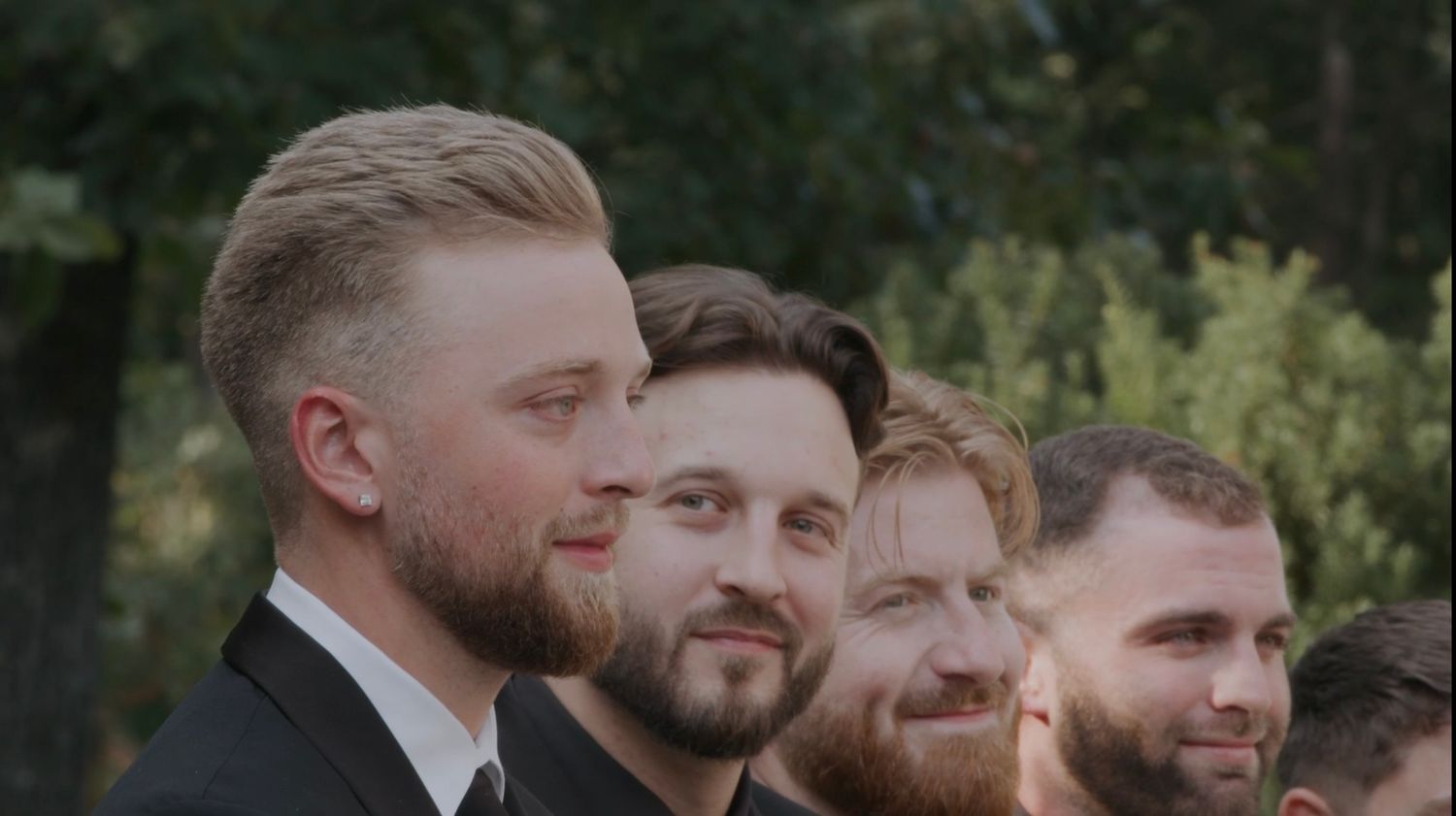 Groomsmen in formal attire standing together outdoors.
