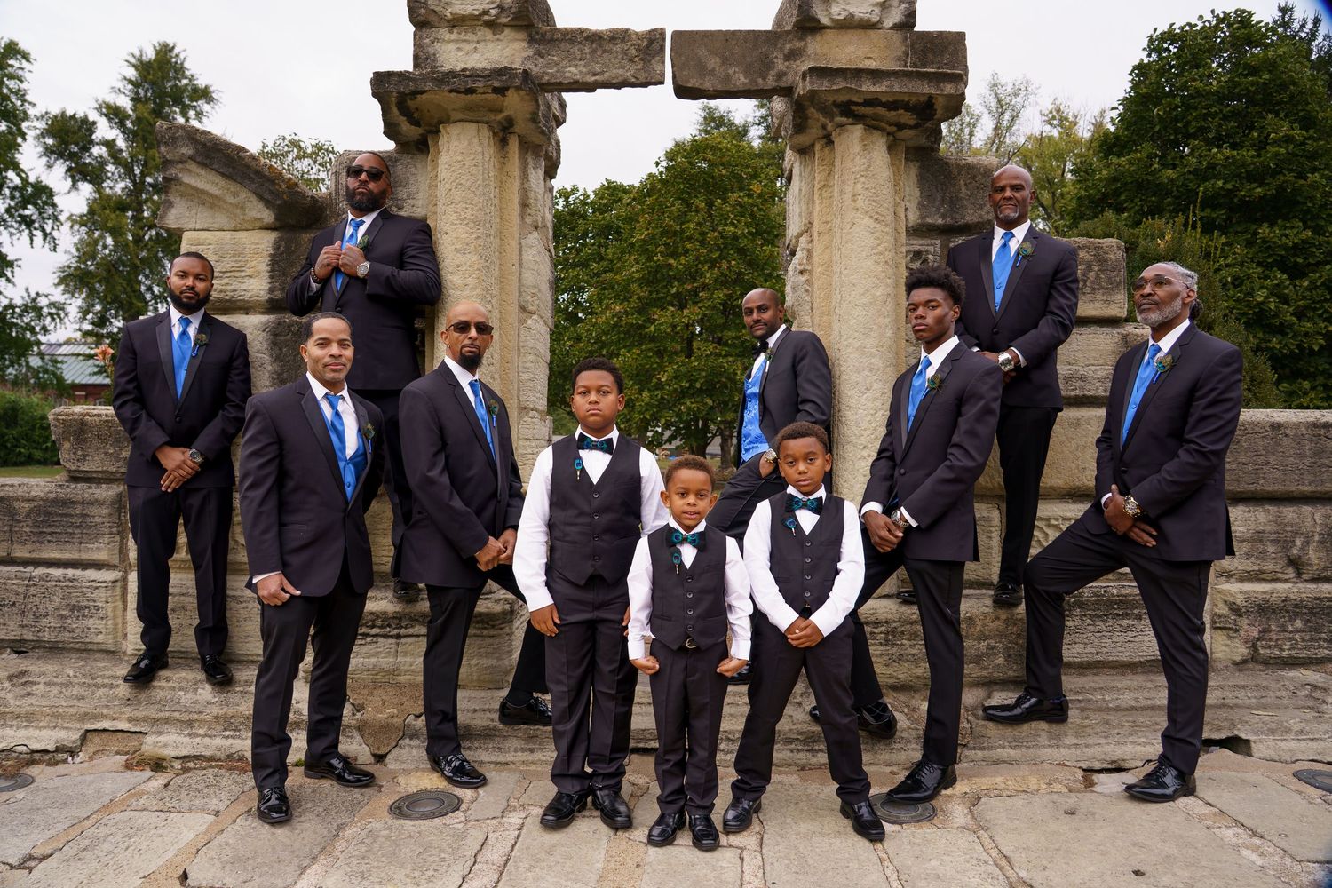 Wedding party poses in formal attire on stone steps with classical architecture in the background.