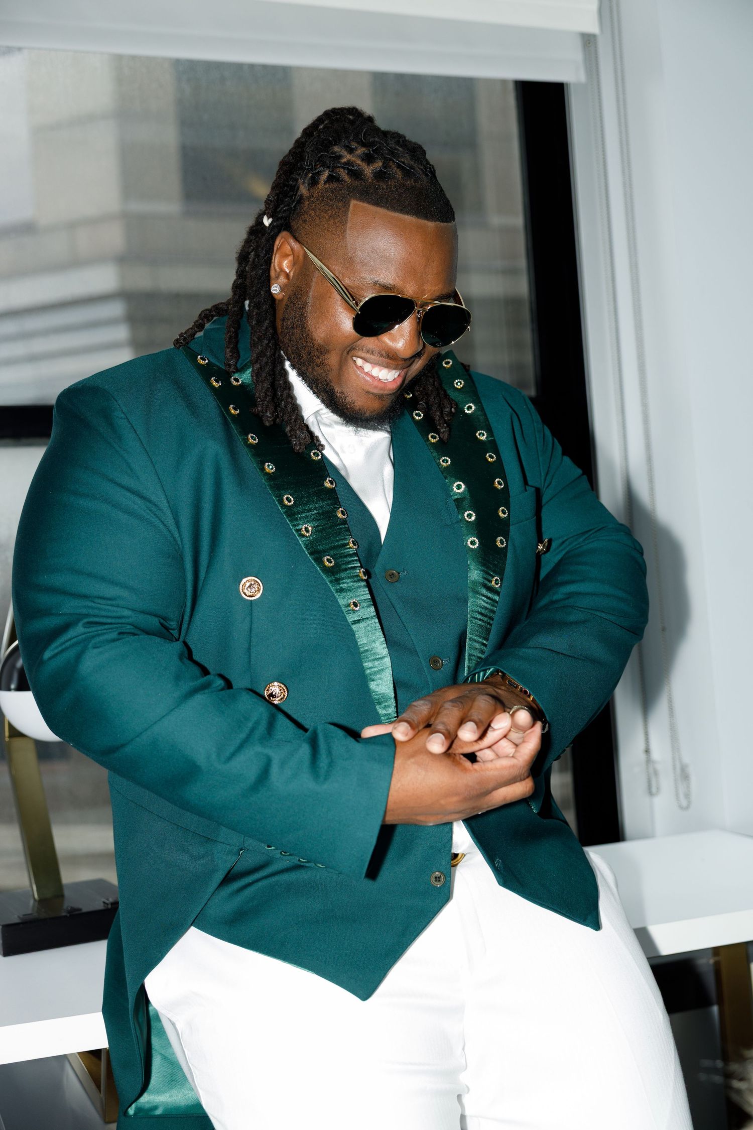 Person wearing emerald green blazer with gold details and sunglasses smiles while looking down.