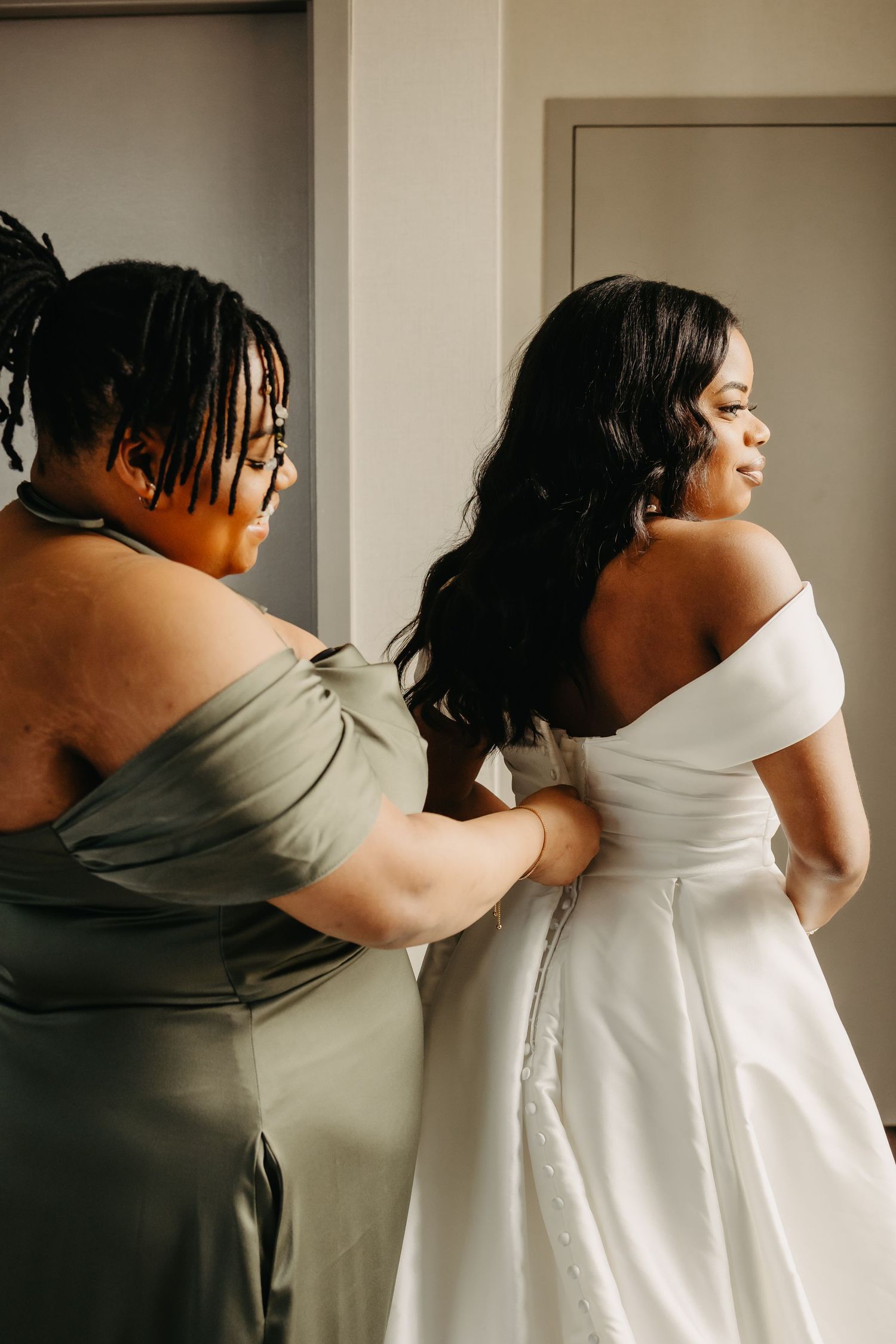 Bridesmaid helping bride with wedding dress in intimate getting ready moment.
