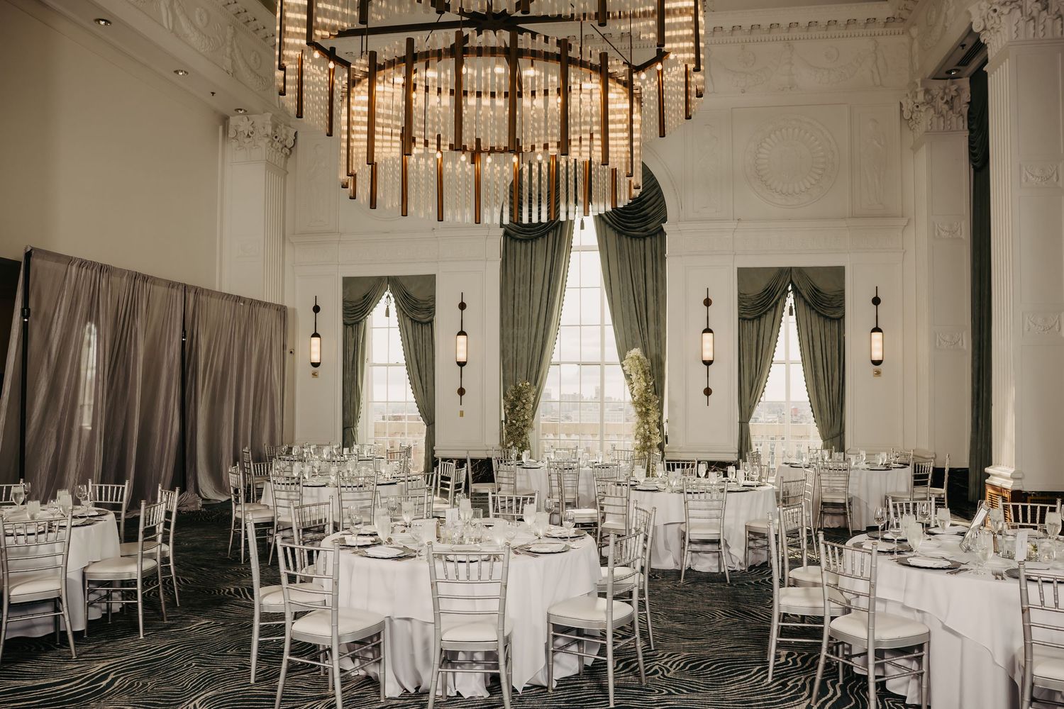 Elegant white wedding reception venue with round tables, chandeliers, and draped fabric creating a romantic atmosphere.