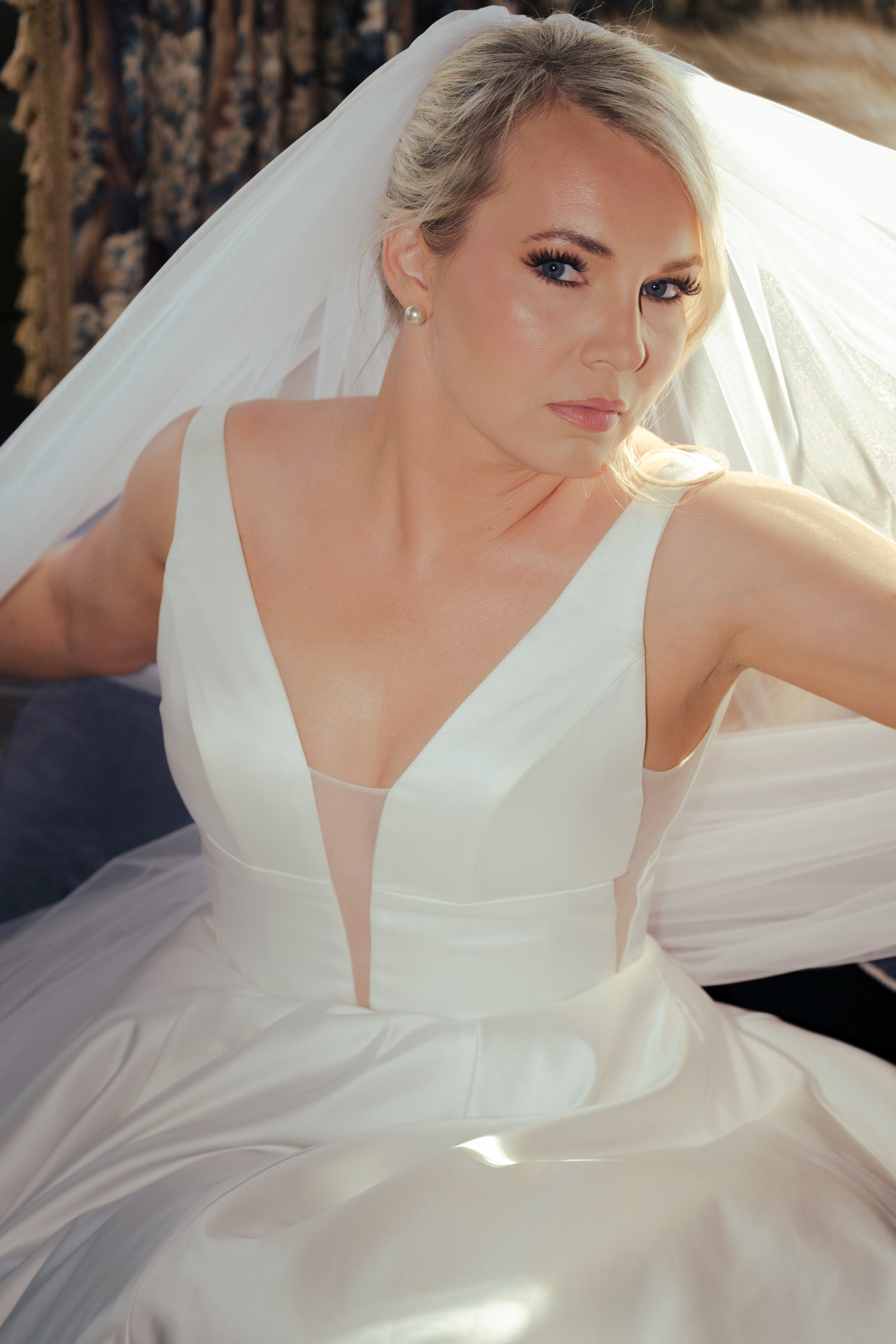 Elegant bride in a white V-neck ball gown with veil, posed gracefully in soft natural light.