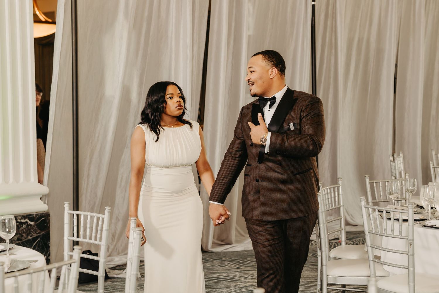 Elegant wedding reception scene with guests dancing in formal attire against white draped backdrop.