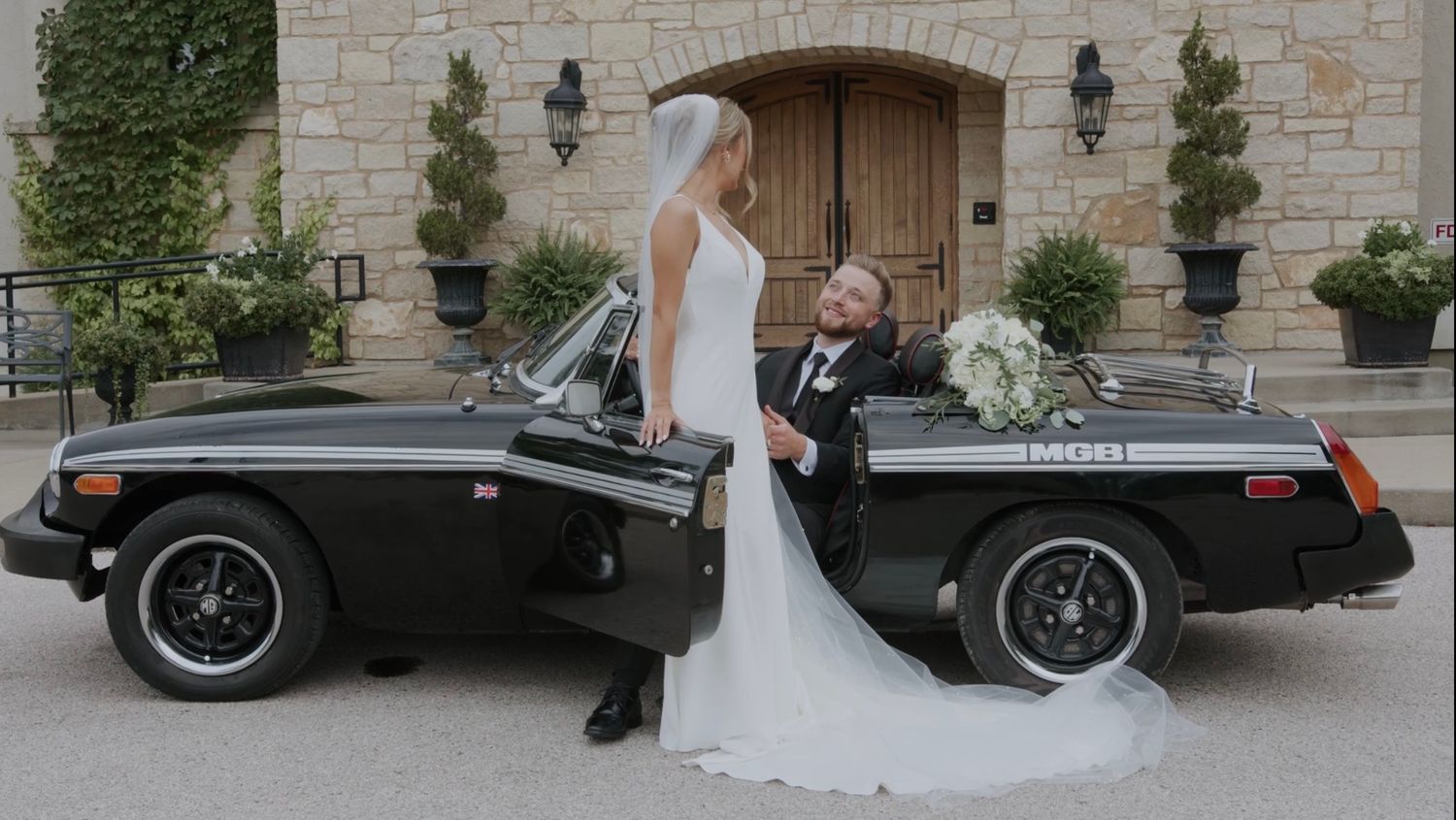 Wedding couple posing with classic black vintage MG convertible car.