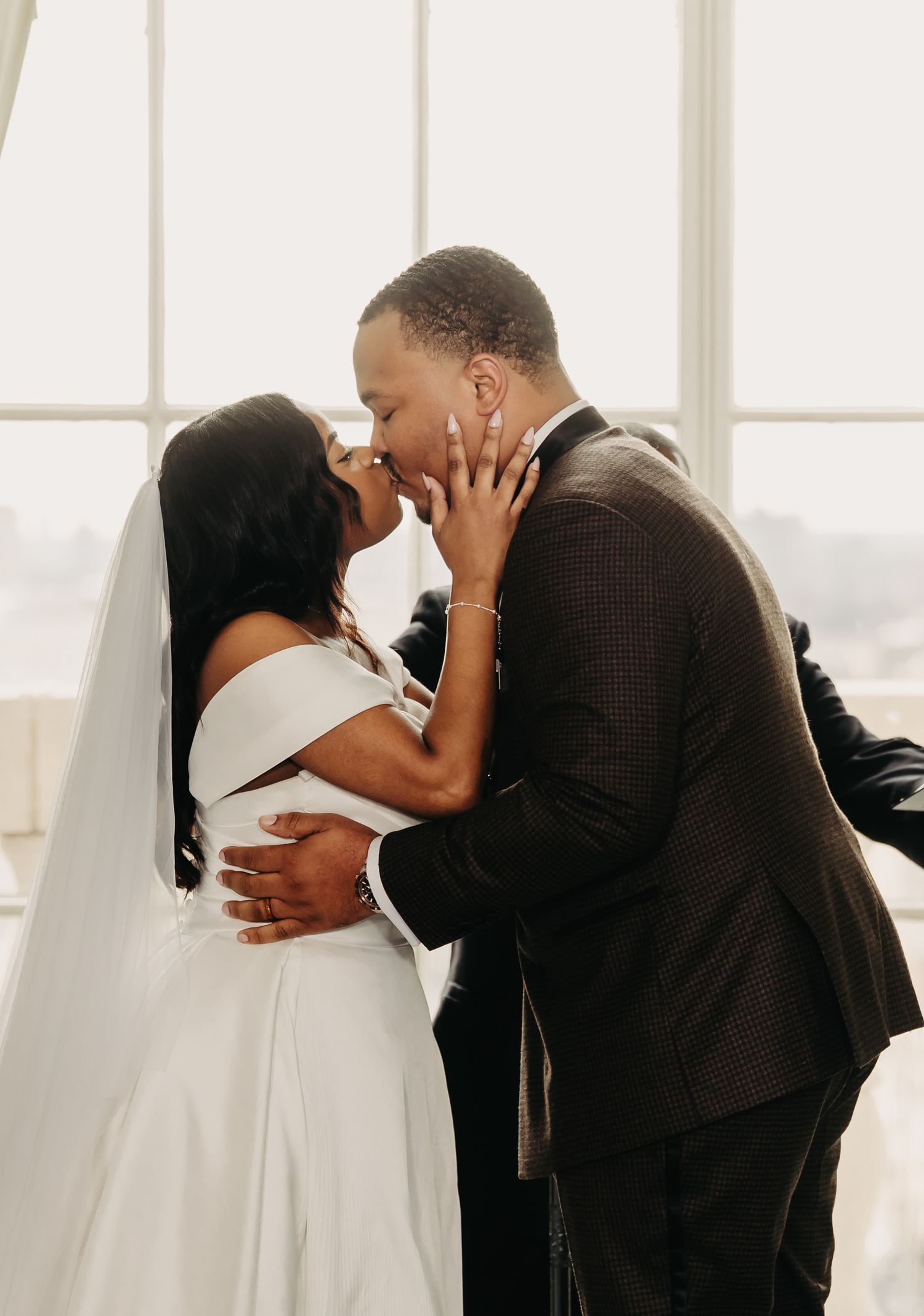 Intimate wedding moment captured in front of bright windows with white drapes.
