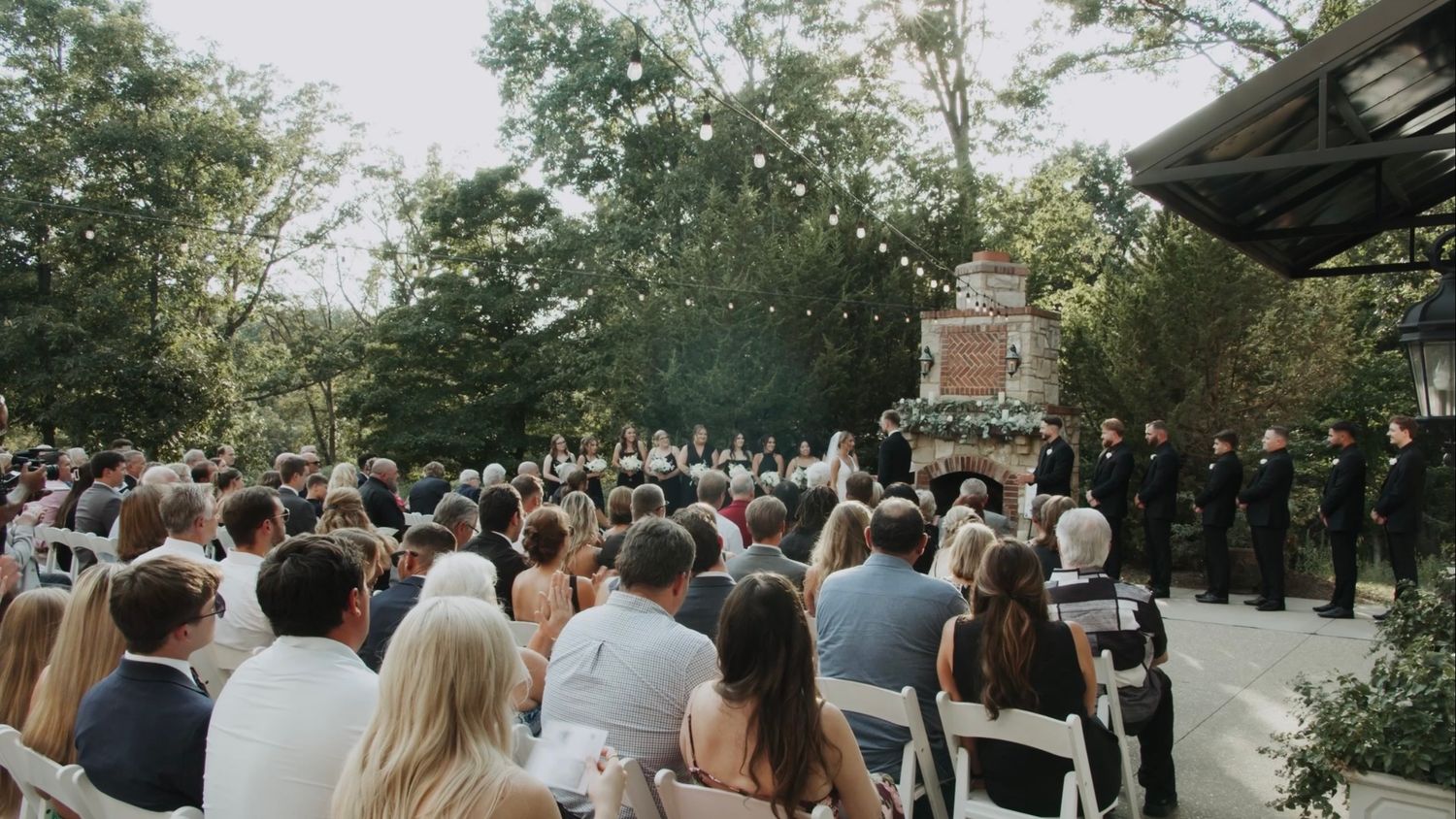 Outdoor wedding ceremony with guests seated in rows under trees.