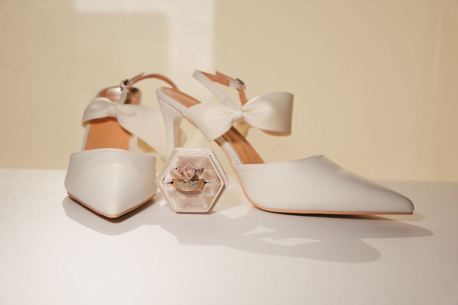 Elegant white bridal shoes and accessories arranged on beige background.