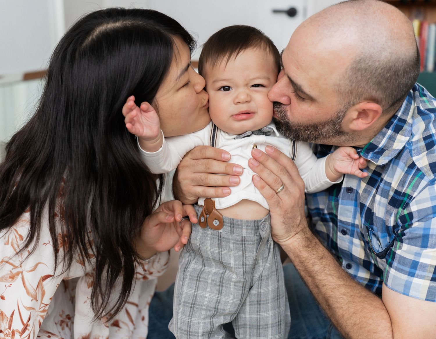 Two parents lovingly kiss their happy baby boy on the cheeks in a warm family portrait.