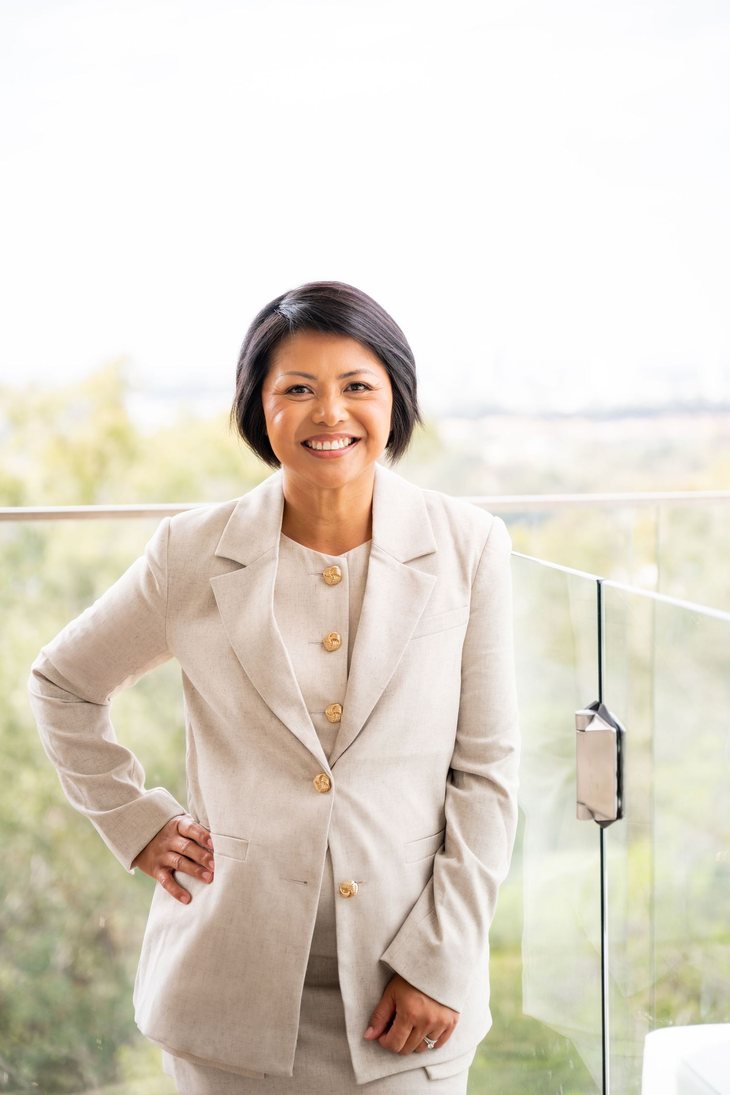 Professional in a cream-colored blazer poses confidently against a bright outdoor background.