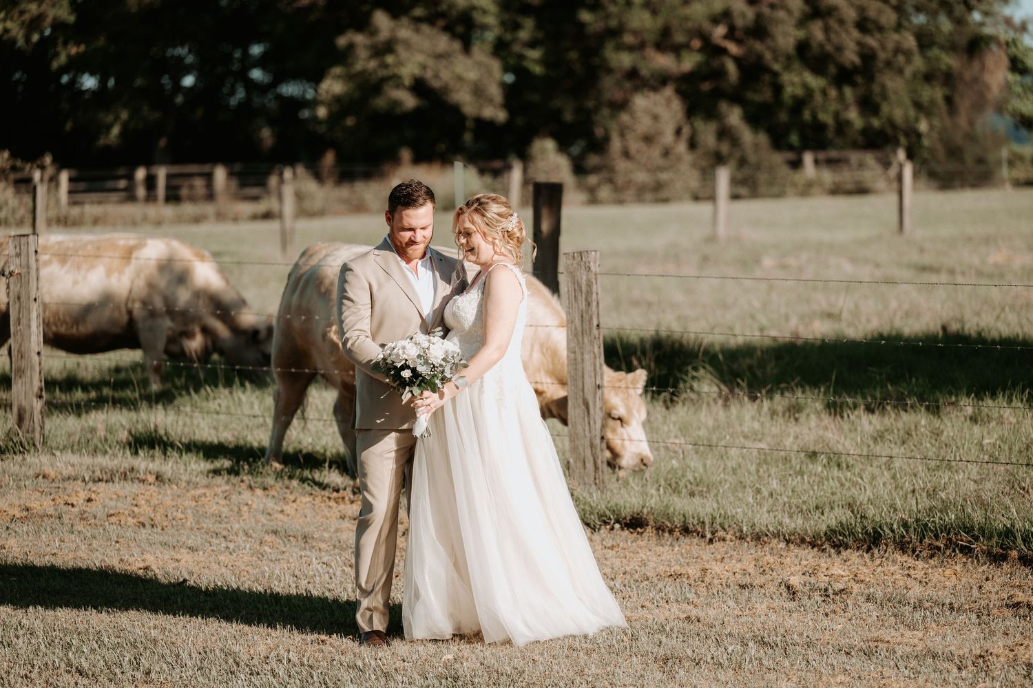 Bride and groom share a romantic moment on a farm with horses grazing in the background on their wedding day.