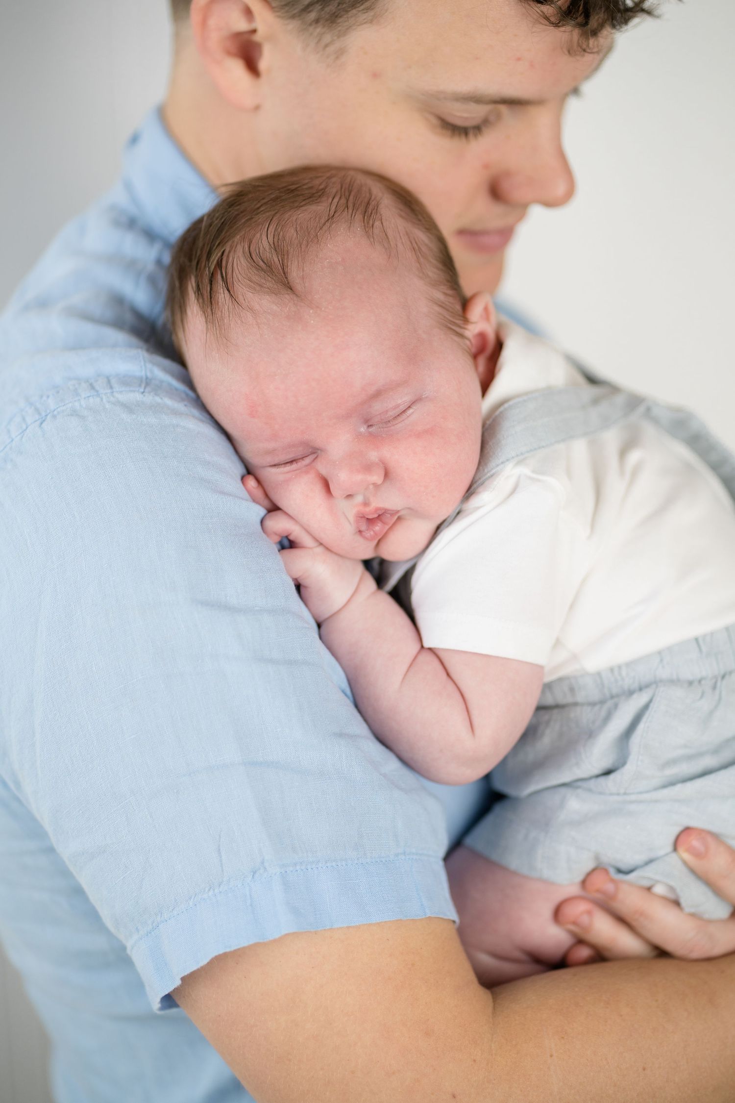Father gently cradling sleeping newborn baby against his chest in a tender bonding moment.