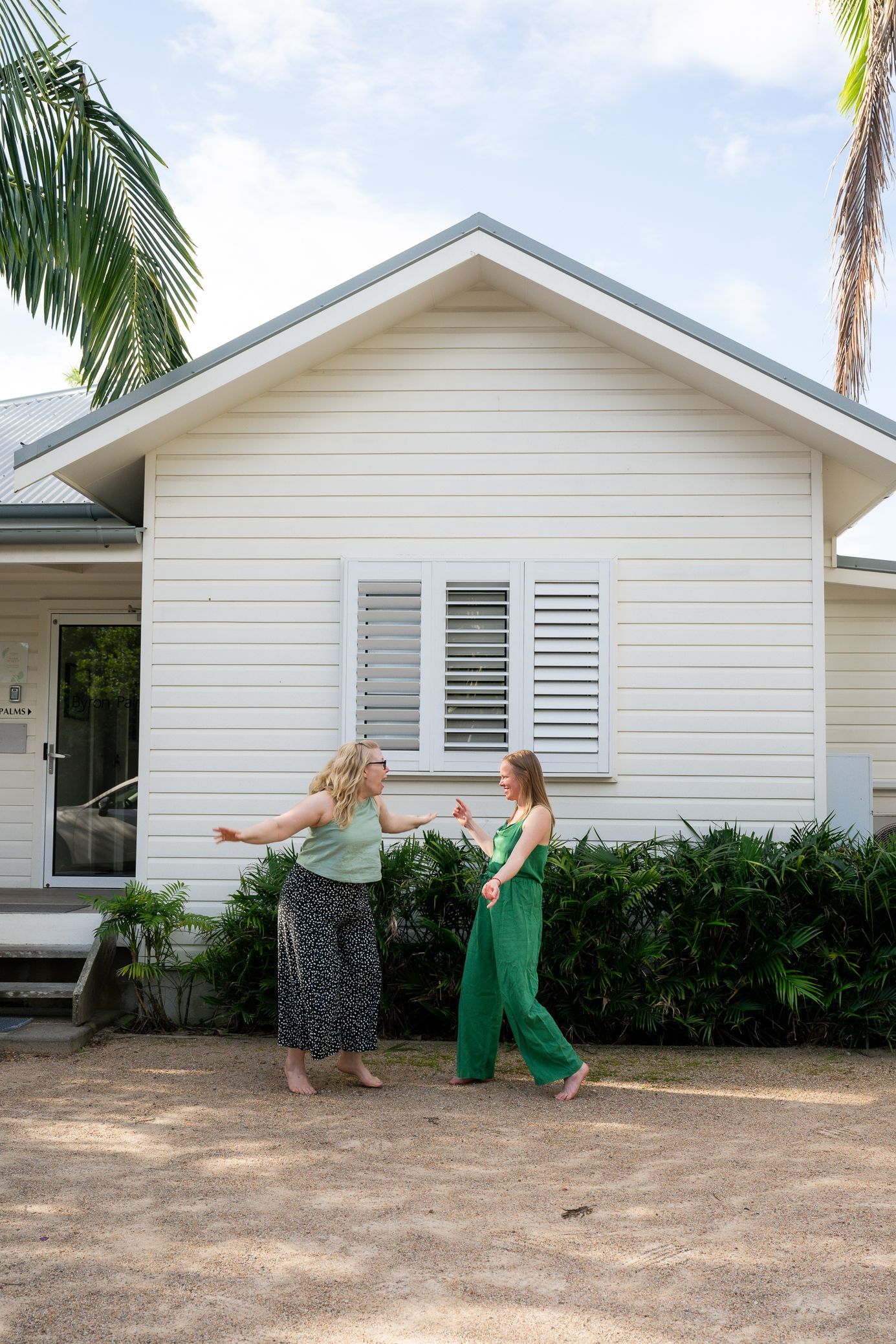 Four sequential shots of people in dresses dancing in front of a white beach house with palm trees.