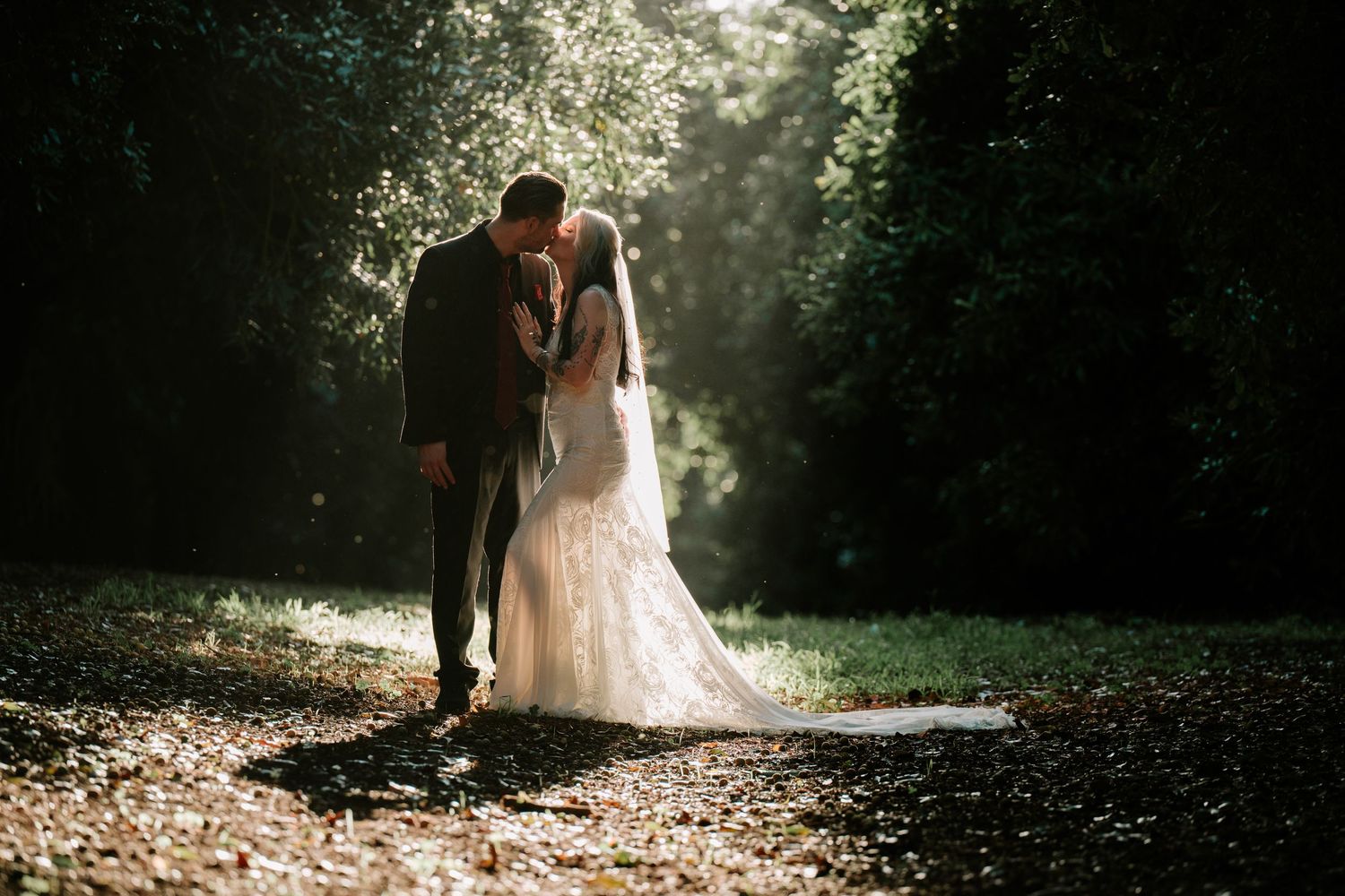 Bride and groom sharing a romantic moment on a sunlit forest path, surrounded by lush green trees on their wedding day.