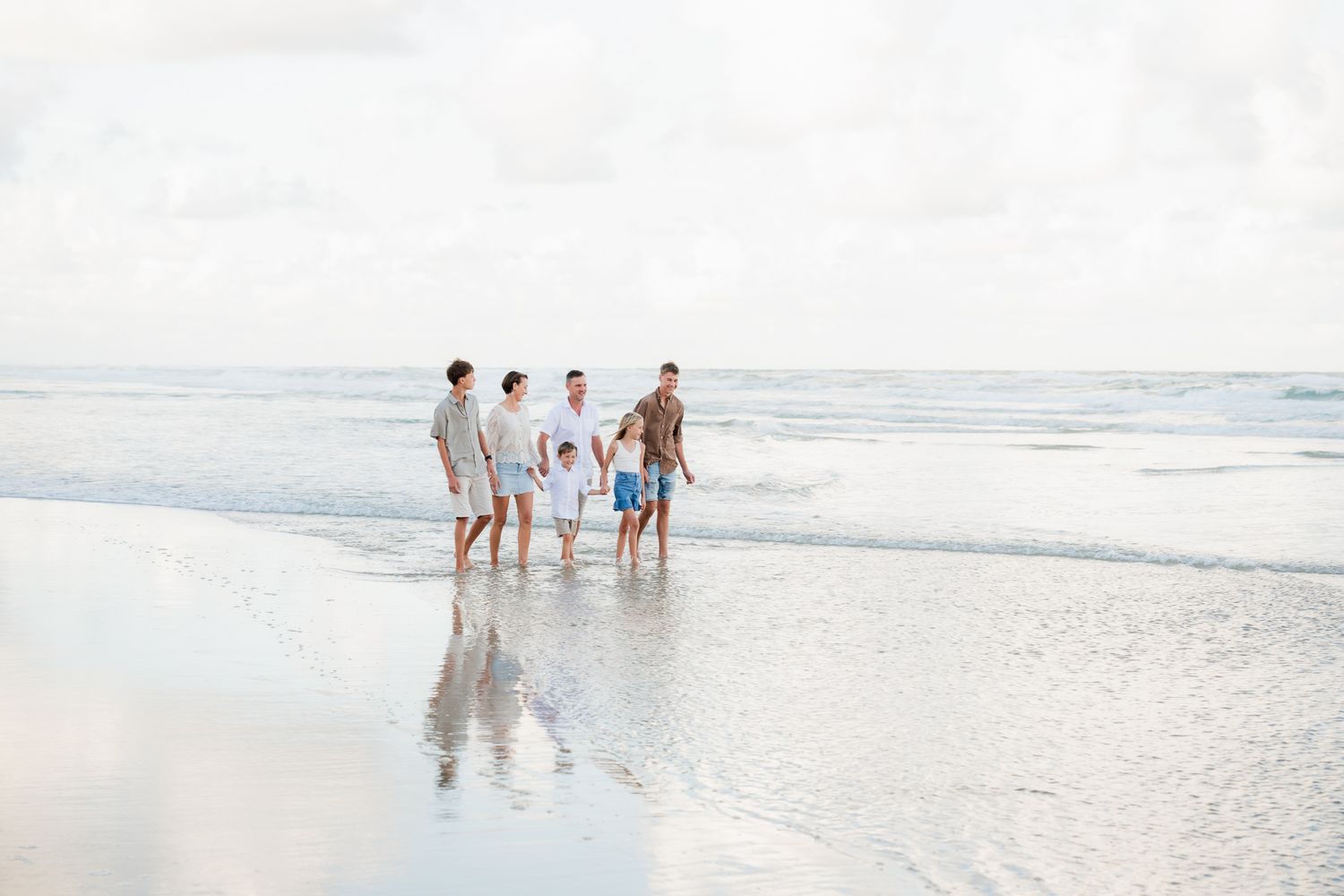 People enjoying a sunny day walking along a pristine white sandy beach with gentle waves rolling in from the ocean.