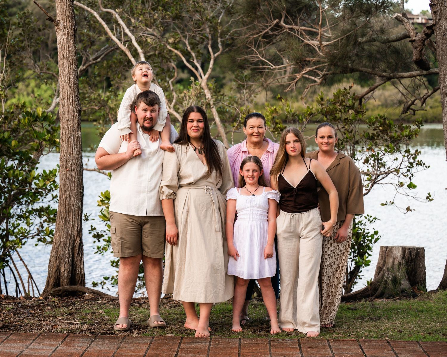 Family of six posing outdoors near a lake surrounded by trees, smiling together for a portrait.