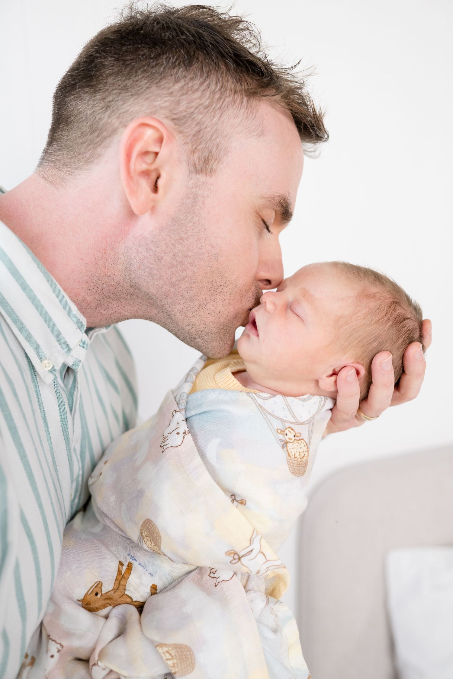 A father tenderly kisses his swaddled newborn baby wrapped in an animal print blanket.