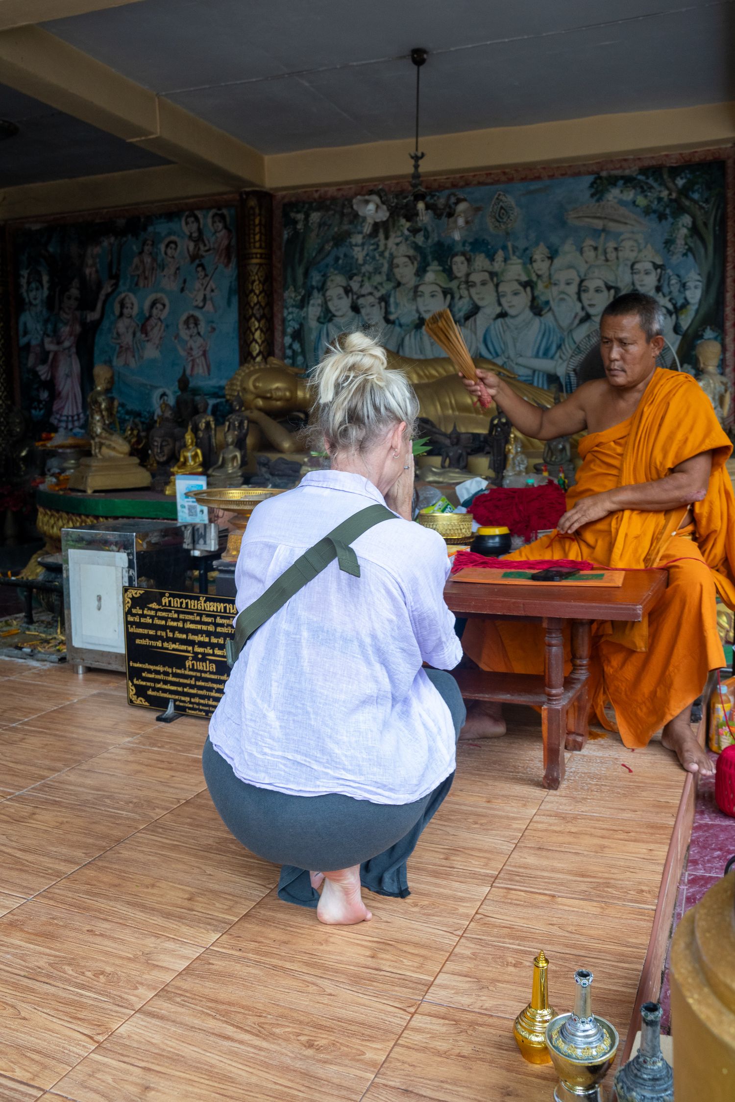 Buddhist monk in orange robes performing a blessing ceremony for a tourist at a temple in Thailand.