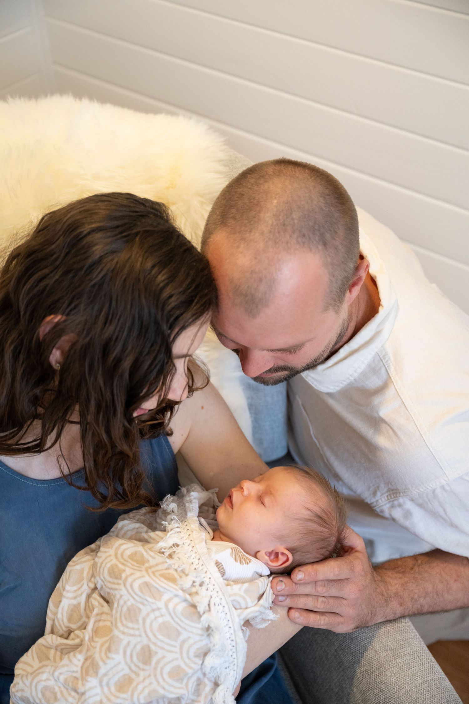 New parents lovingly gaze at their sleeping newborn baby wrapped in a white lace blanket.