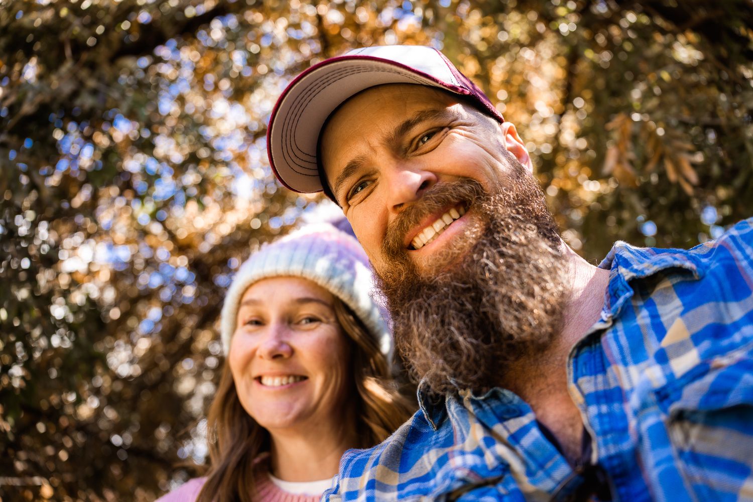 A couple smiles warmly at the camera while enjoying time outdoors in natural lighting.