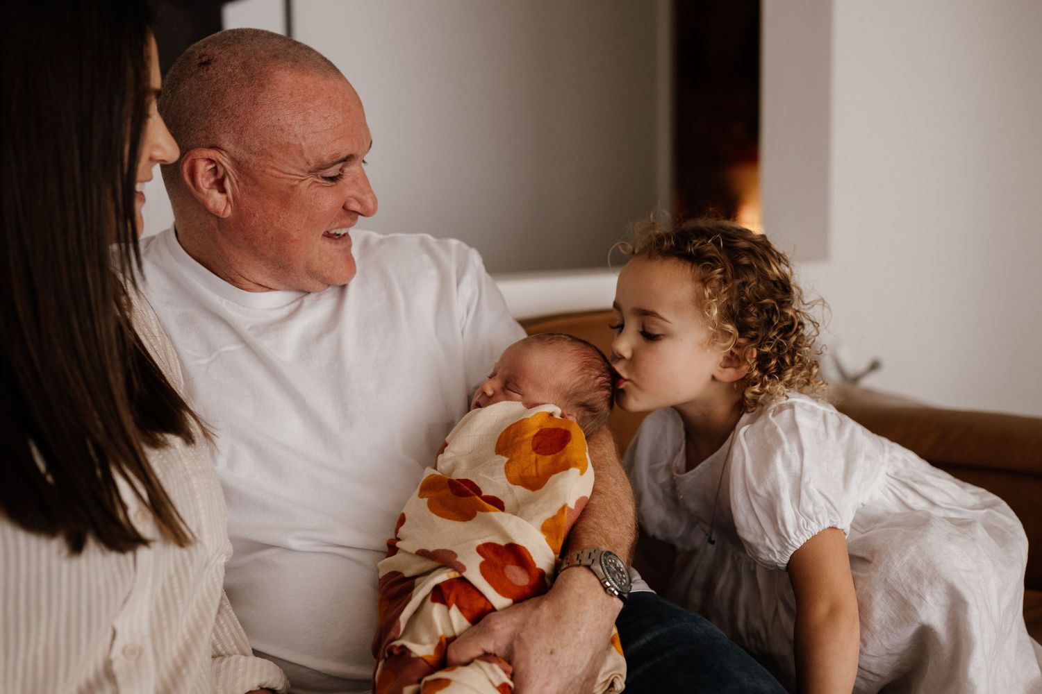 Family members share joyful moments together while sitting on a couch in white t-shirts.
