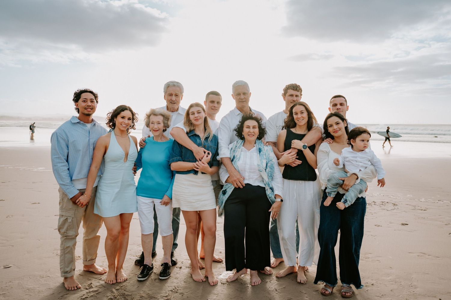 Large family group posing together on a beach, smiling for a portrait with ocean waves in the background.