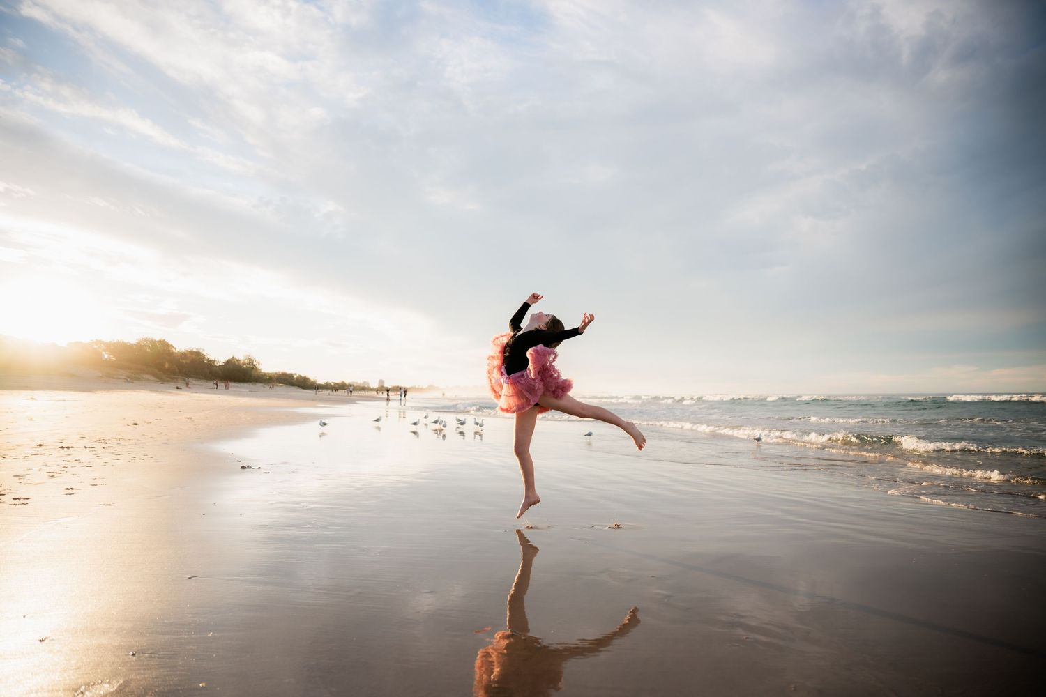 Silhouetted figure dancing gracefully on a sandy beach at sunset with waves crashing in the background.