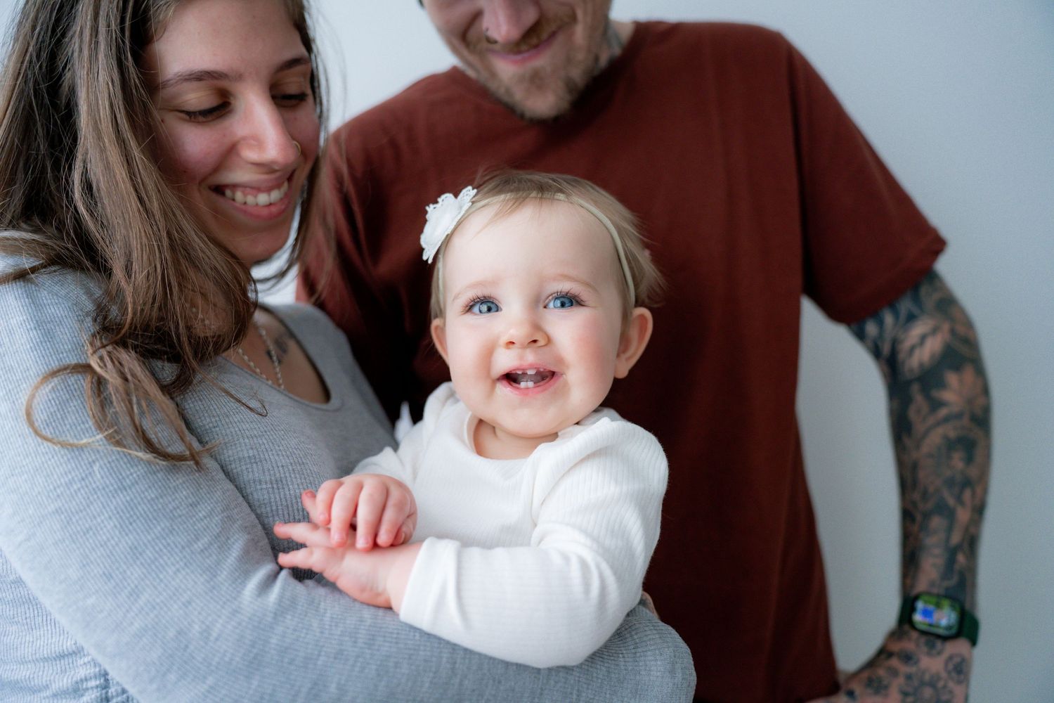 Parents holding their toddler in Banora Point studio, Dad has tattoos and mum and baby laughing with Wonderland Photography