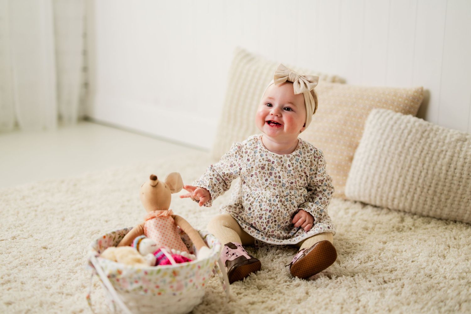 Happy baby girl sitting on a fluffy carpet, laughing and playing with toys beside a cozy couch.