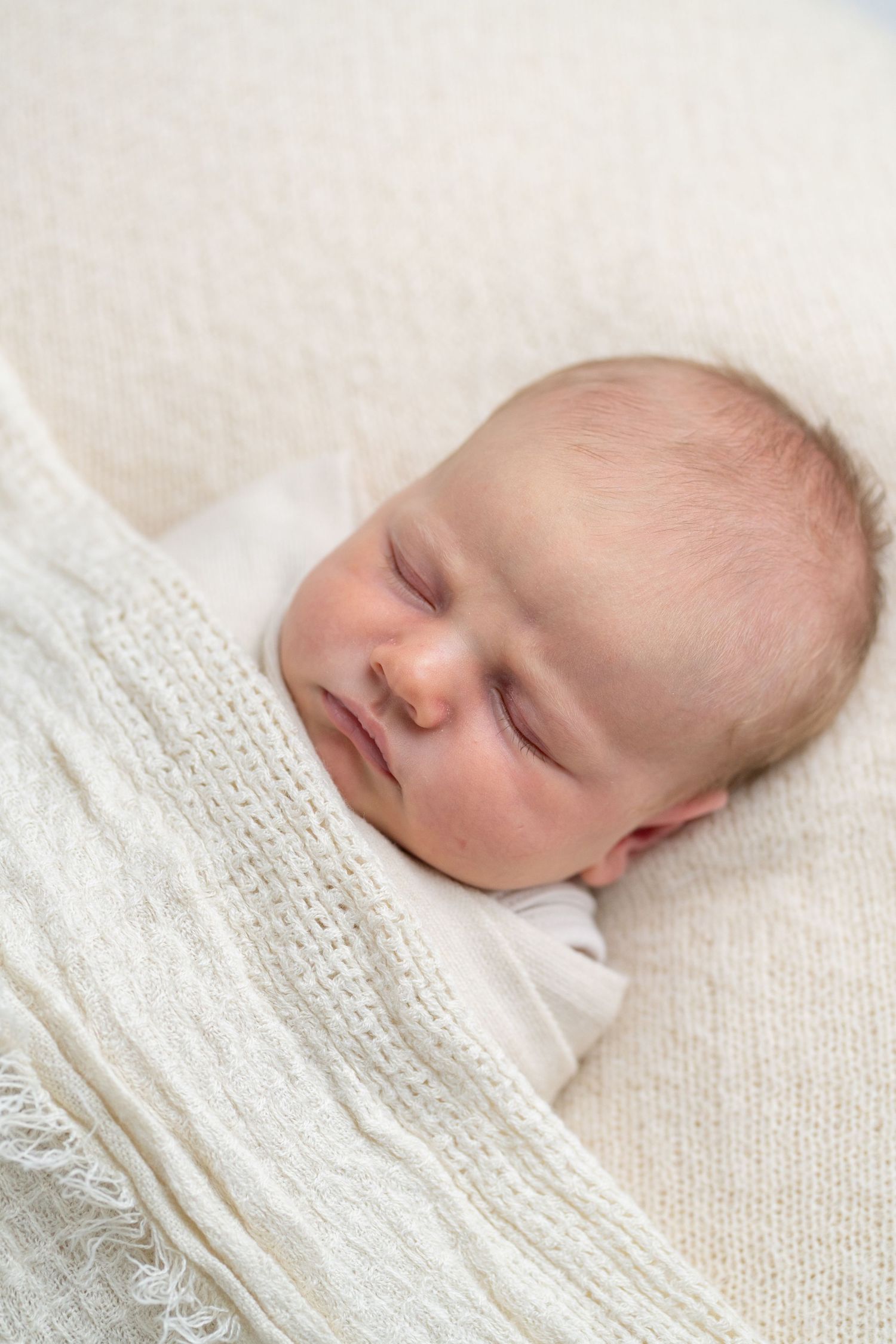 Peaceful newborn baby sleeping soundly wrapped in a soft white knit blanket.