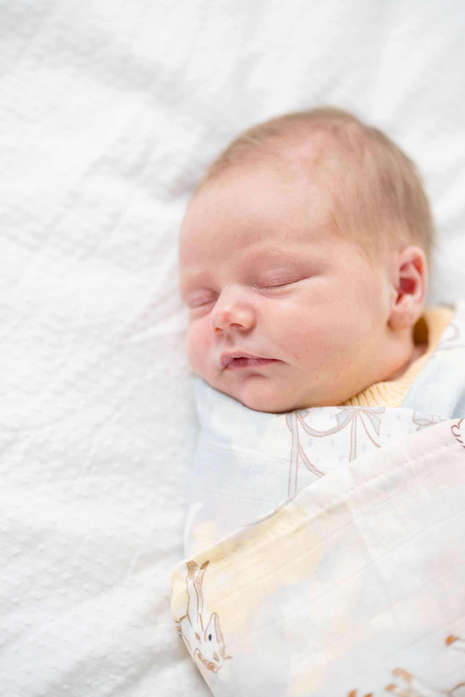 Peaceful newborn baby sleeping soundly, swaddled in a soft blanket with bunny print on white bedding.