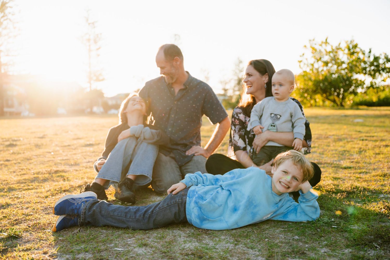 Family of five enjoying golden hour outdoors at Kingscliff on grass, parents with three young children smiling in warm sunlight.