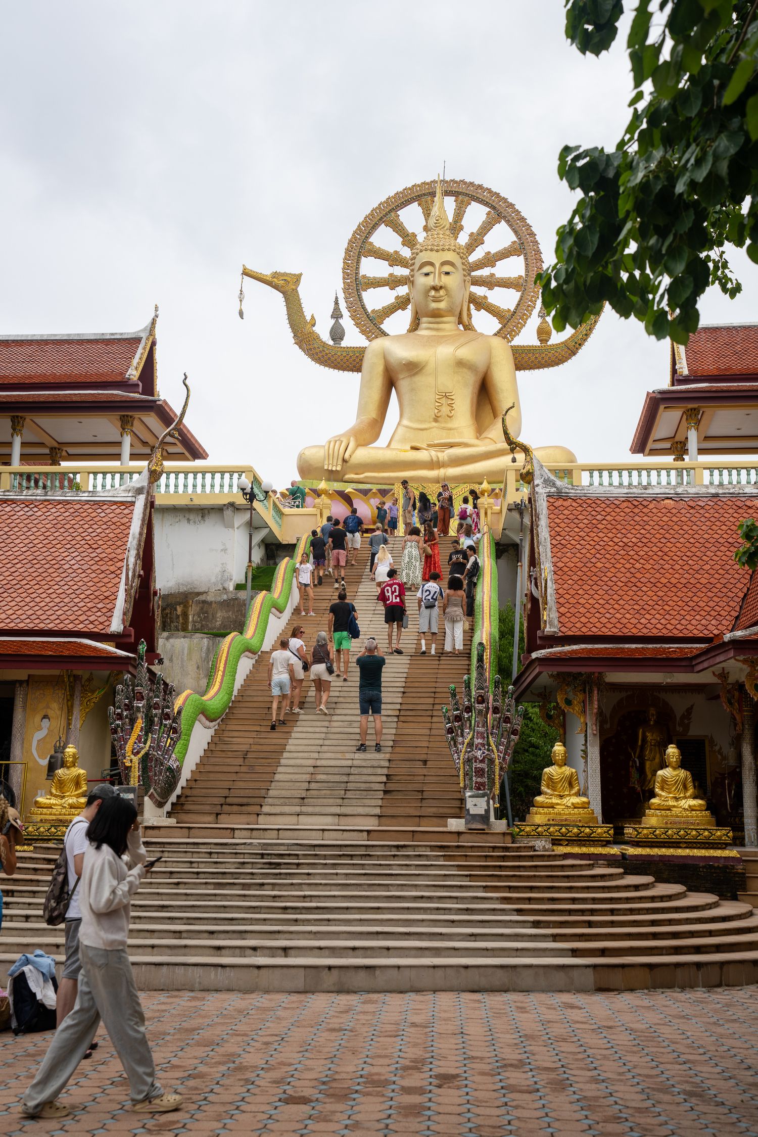 Tourists climbing steps to the golden Big Buddha statue at Wat Phra Yai temple on Koh Samui, Thailand.