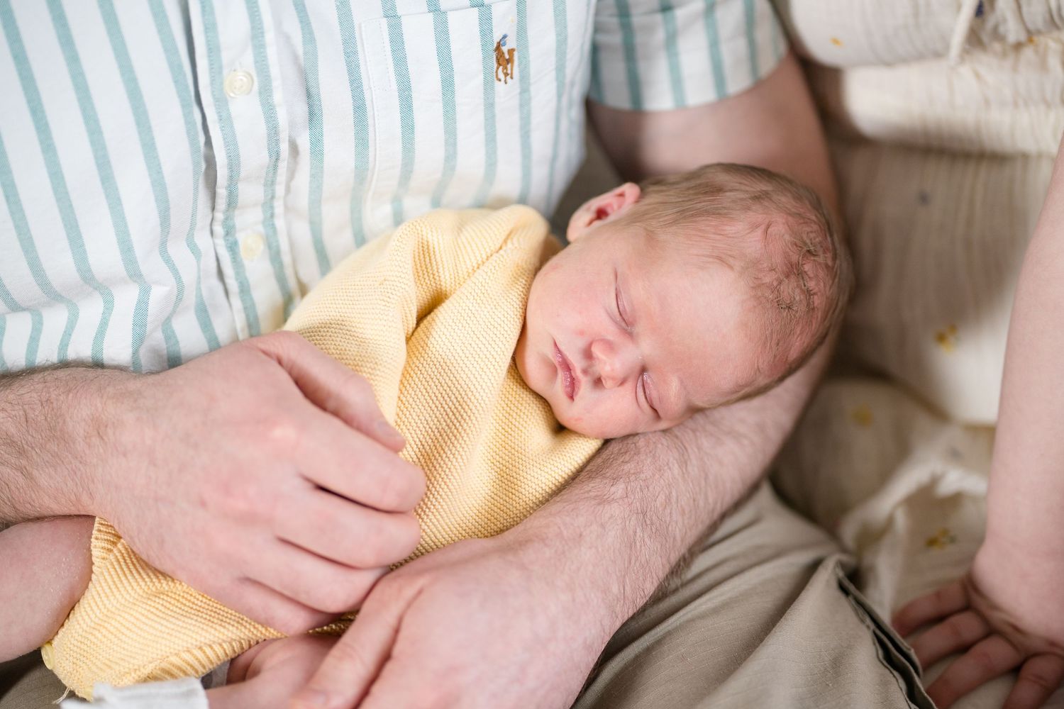 Newborn baby sleeping peacefully in yellow onesie cradled in parent's arms.