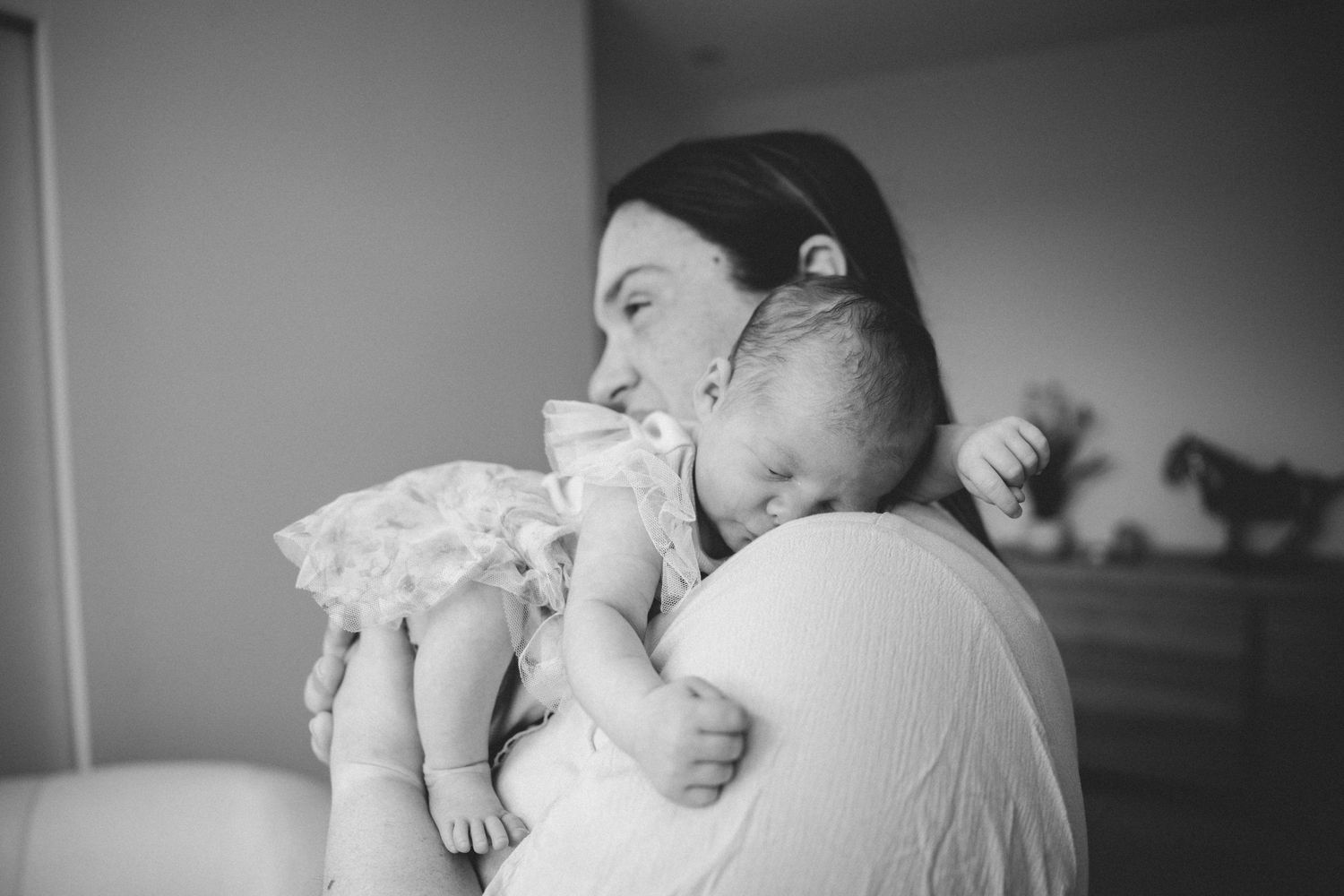 A tender black and white photograph of a parent cradling and kissing a sleeping baby in a quiet room.