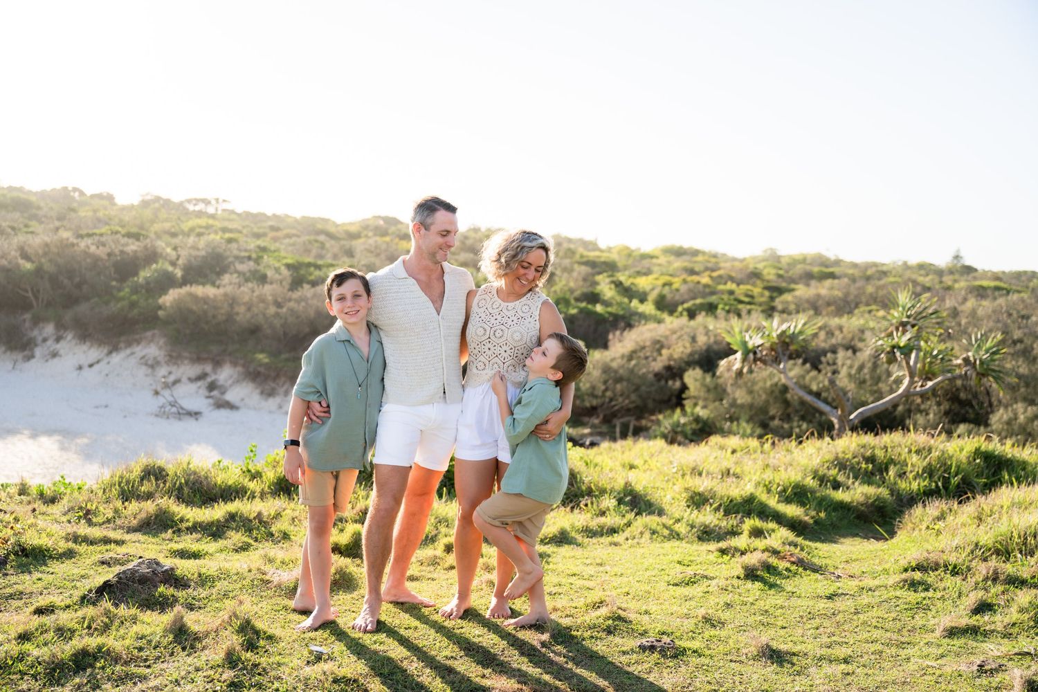 Family of four posing together on a grassy coastal dune on a sunny day.