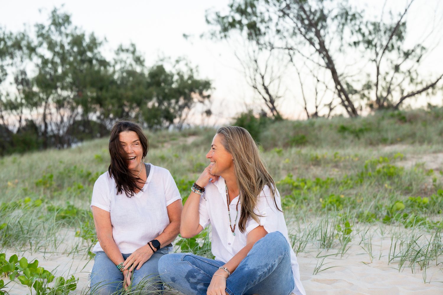 Two people in casual attire share joyful moments while sitting together on a sandy beach.