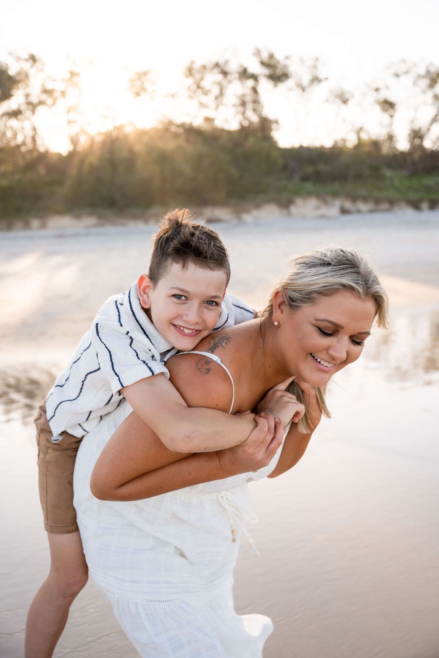A playful moment captured on a beach at sunset with a white dress and casual attire.