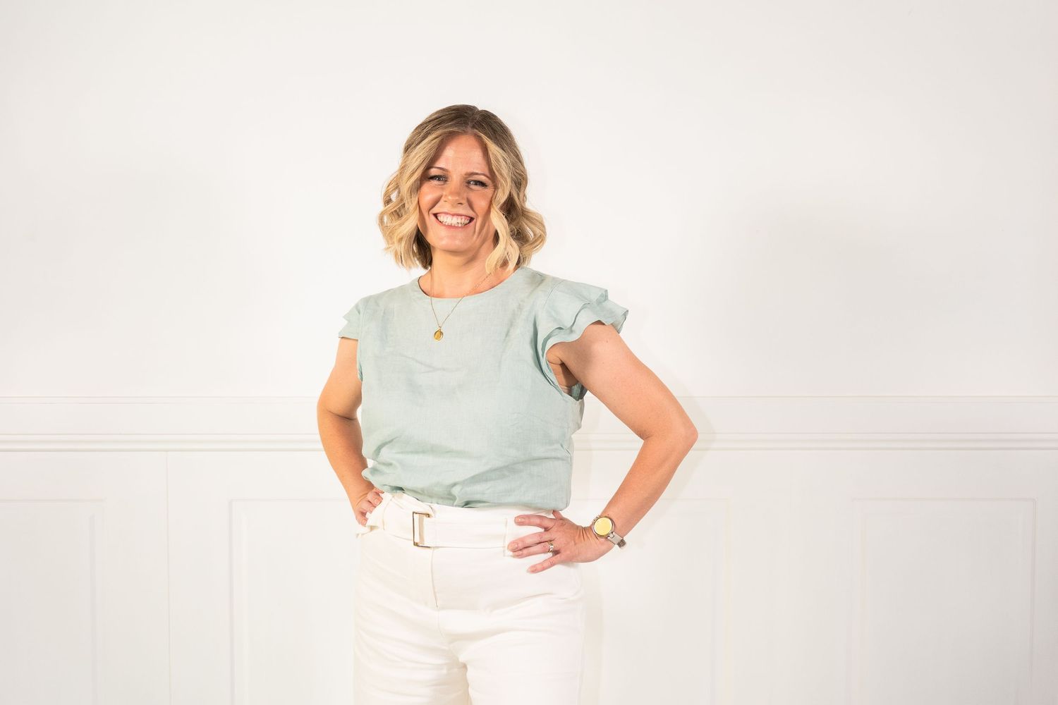 A person in a mint green t-shirt and white pants poses confidently against a light background.