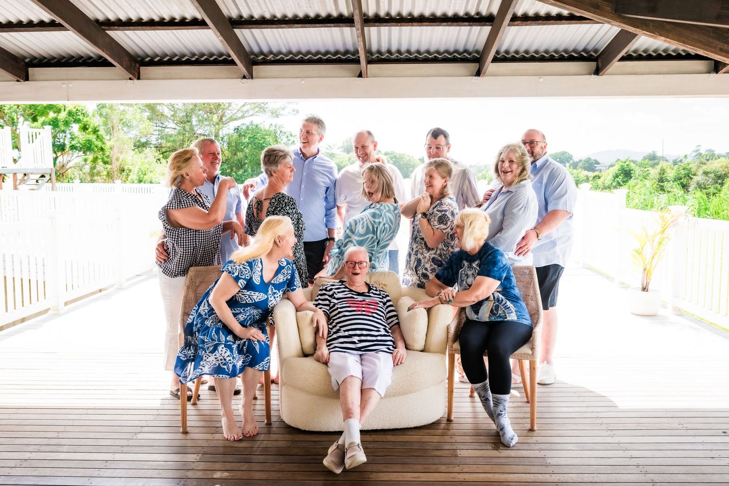 Large family group portrait on a covered outdoor deck, with adults seated and standing, smiling together.