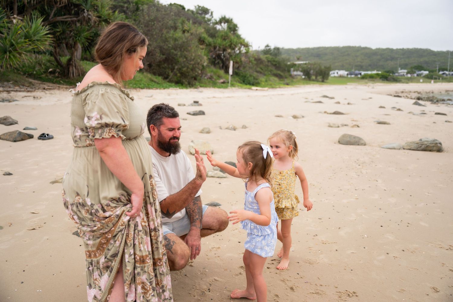 Family of four enjoying a fun moment together on a sandy beach, with two young girls and their parents.